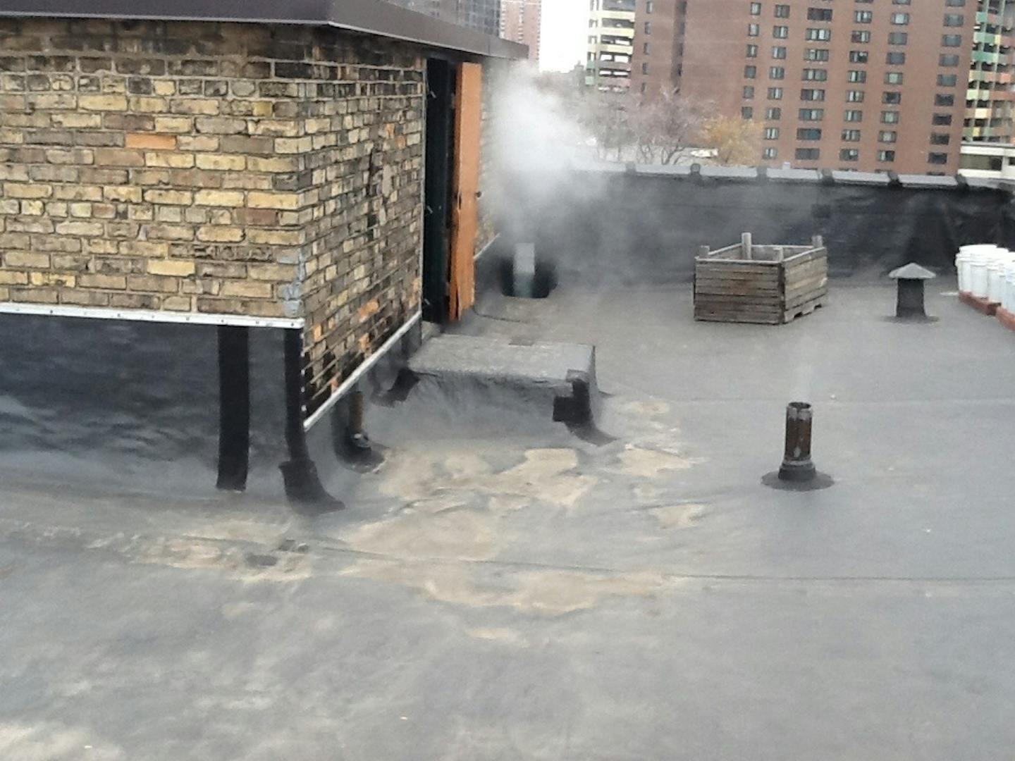 A sanitary exhaust vent atop a flat-roofed building, during smoke testing, which can't be spotted easily from the ground.