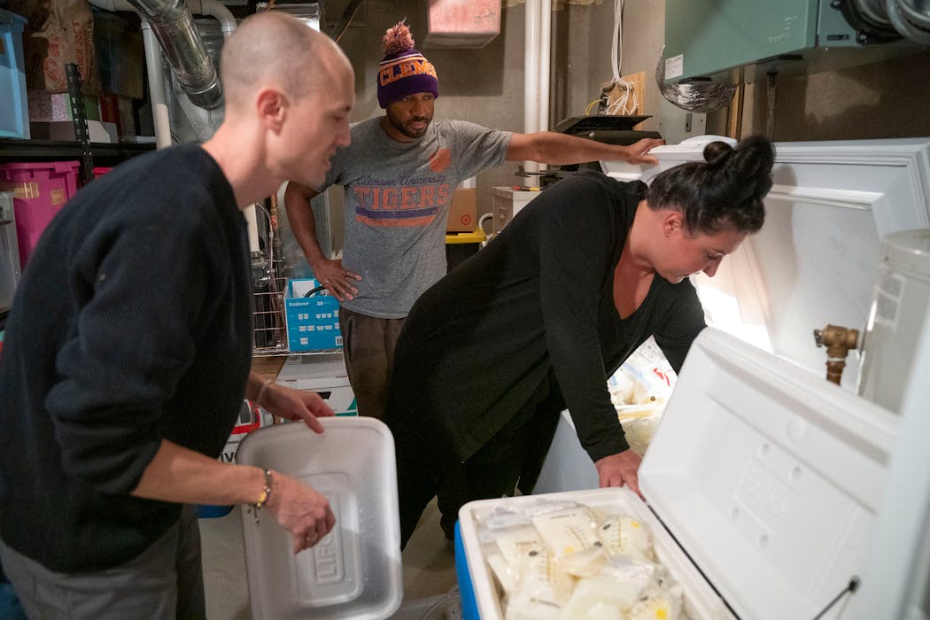 Seth Snyder gets help from his neighbors, Dwayne Toatley and Heather Axtman, as they stock two coolers with donated breast milk from the couple’s deep freezer. Axtman organized a breast milk collection drive that has taken up contributions from more than 20 pumping moms.