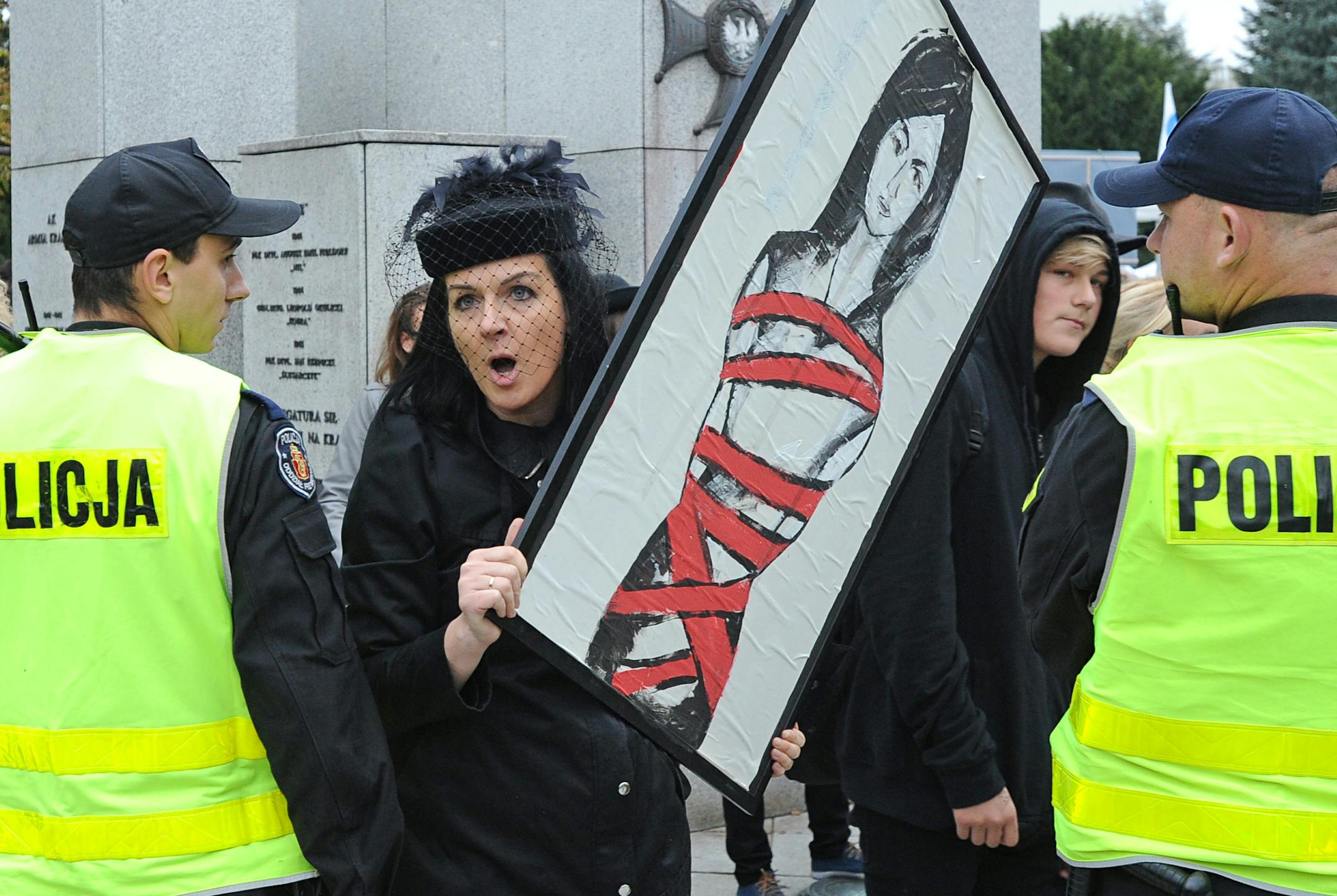 A pro abortion protester, dressed in black to signify grief in terms of the abortion ban, shouts slogans towards supporters of the abortion ban, as she is guarded by police officers in front of the Polish parliament, in Warsaw, Poland, Thursday, Sept. 22, 2016. Lawmakers on Thursday began discussing a draft supported by the conservative government that calls for a total ban on abortions, and another by the opposition seeking to allow abortions through the 12th week of pregnancy. (AP Photo/Alik K