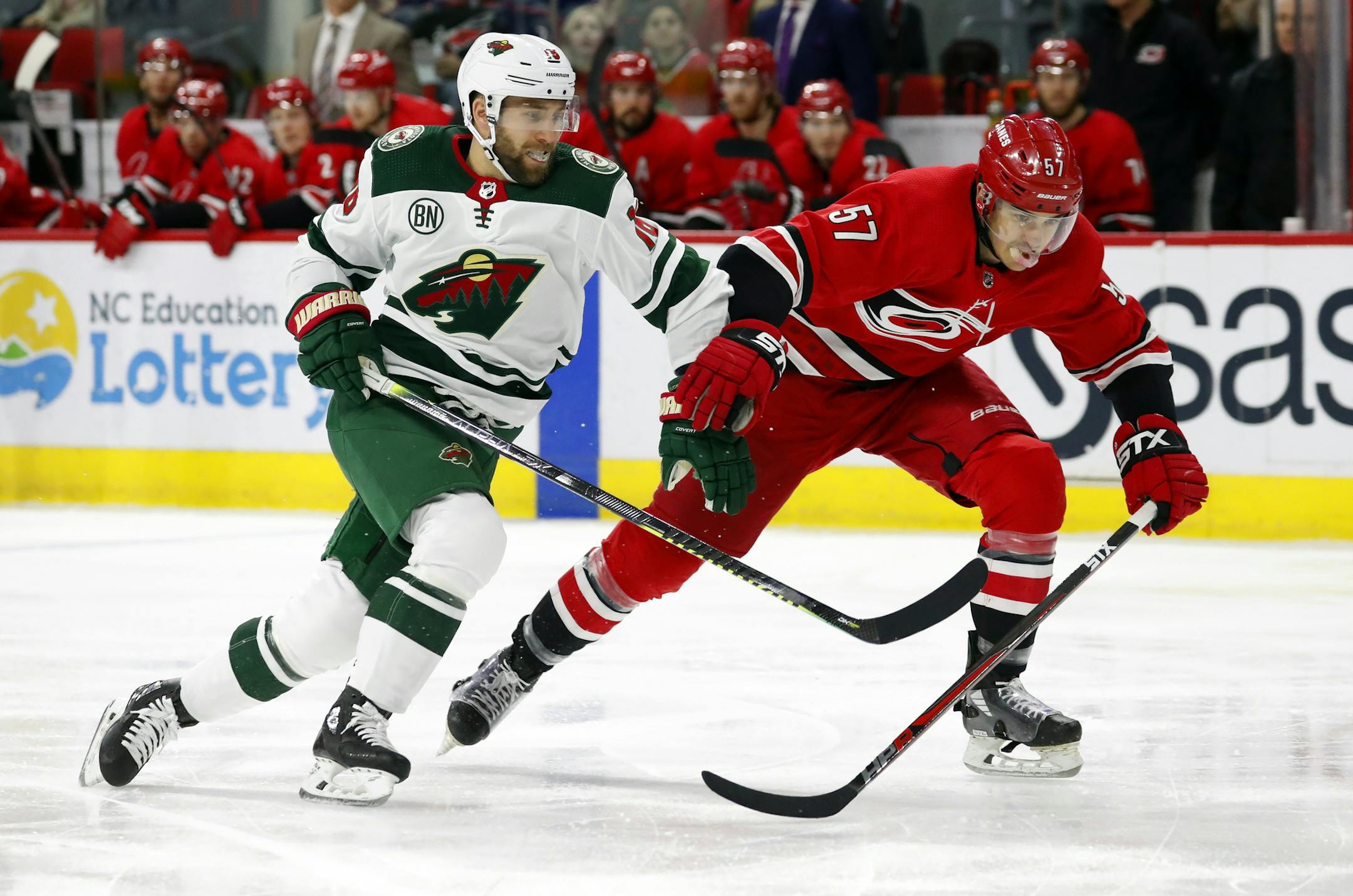 Minnesota Wild's Jason Zucker (16) chips the puck ahead of Carolina Hurricanes' Trevor van Riemsdyk (57) during the first period of an NHL hockey game, Saturday, March 23, 2019, in Raleigh, N.C. (AP Photo/Karl B DeBlaker)