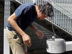 A young man tries to cool off with help from a drinking fountain.