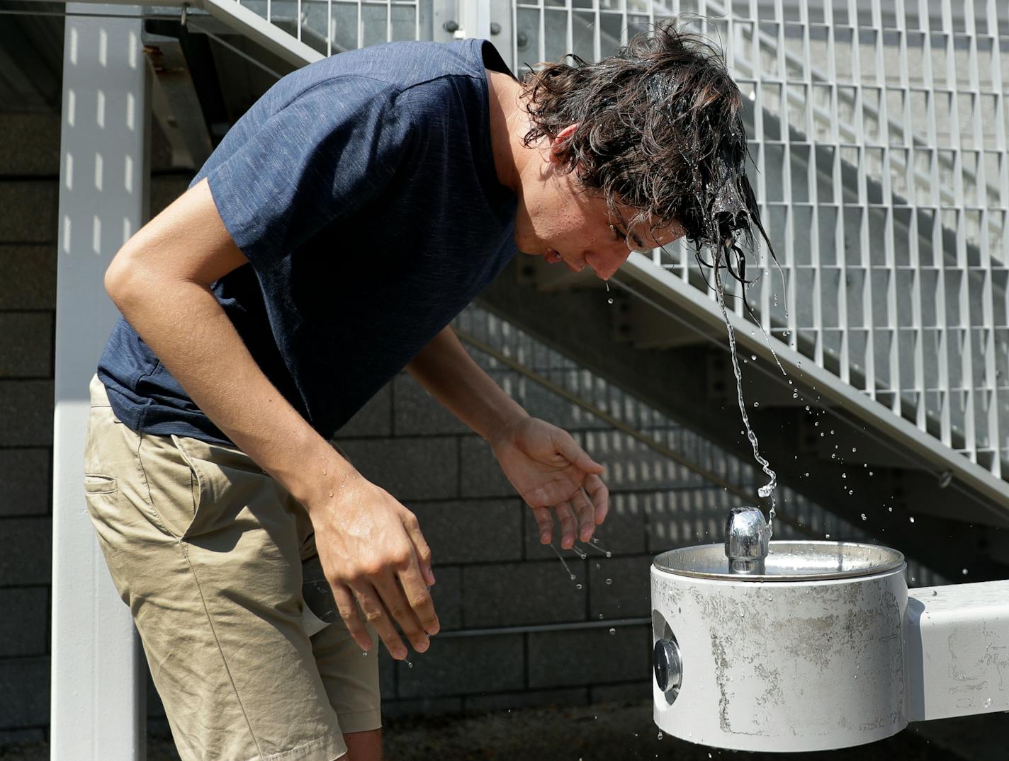 A young man tries to cool off with help from a drinking fountain.