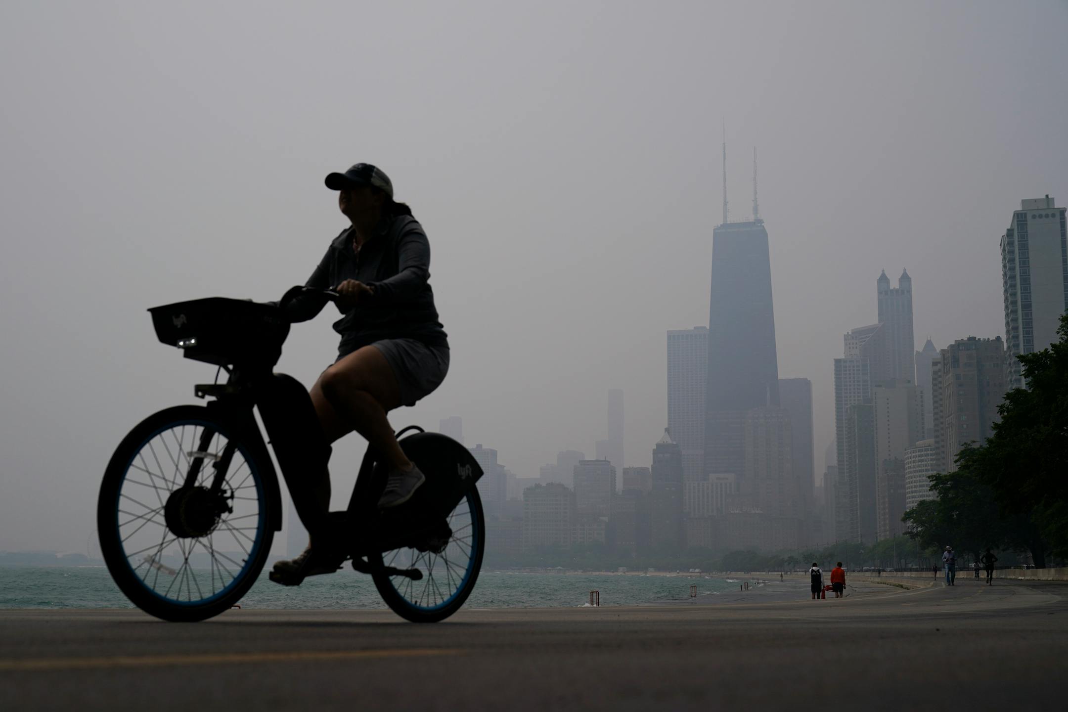 A person rides a bicycle along the shore of Lake Michigan as the downtown skyline is blanketed in haze from Canadian wildfires in Chicago.