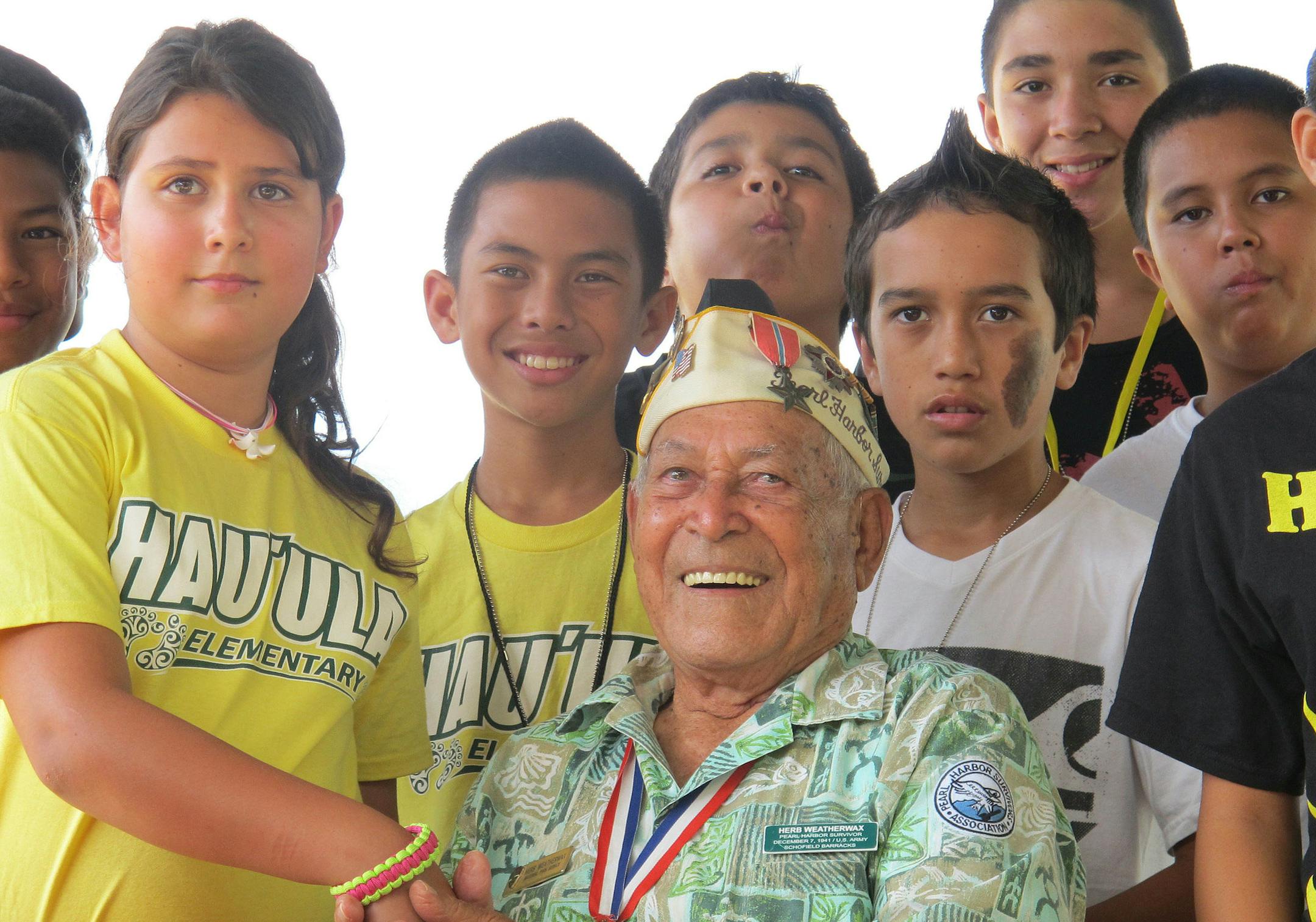 In this photo taken Nov. 22, 2013, Herb Weatherwax, seated, poses for a photo with Hauula Elementary School sixth graders from left Dawson Langinbelik, Rachel Cheney, Frank Kojima, La'a Beatty, Chase Colleado, Makoa Ahquin-Soren and Keola Baily in Pearl Harbor, Hawaii. The 96-year-old retired electrician is one of four Pearl Harbor survivors who volunteers to greet visitors at the historic site. On Saturday is the 72nd anniversary of the 1941 attack by Japan on Pearl Harbor. (AP Photo/Audrey McA