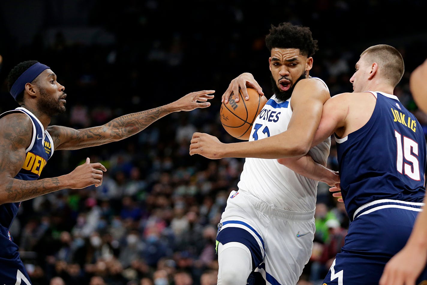 Minnesota Timberwolves center Karl-Anthony Towns (32) drives on Denver Nuggets center Nikola Jokic (15) and forward Will Barton during the first half of an NBA basketball game Tuesday, Feb. 1, 2022, in Minneapolis. (AP Photo/Andy Clayton-King)