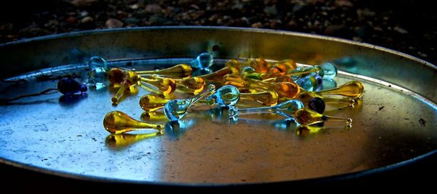 Beads from blue and yellow glass lay in a pan, and later Reynolds will twist wire around the small ball and make jewelry.