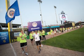 Randy Hall held the Minnesota Flag and Joan Boger held a Minnesota sign as they lead more than a hundred Minnesota athletes onto CHS Field during the 