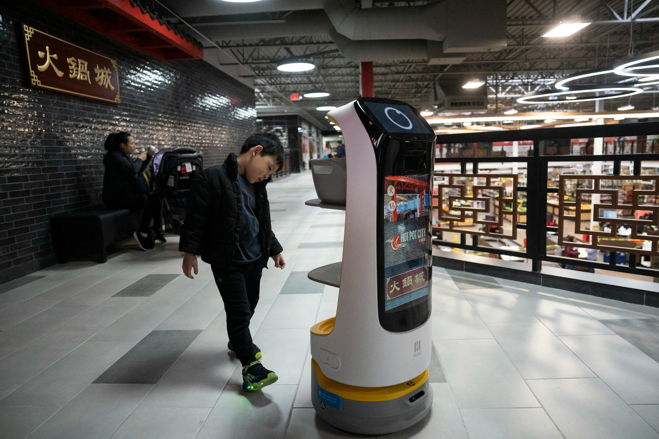 Kun Shi, 5, follows a robot that was handing out menus for the restaurant Hot Pot City at a soft opening for the new Asia Mall.