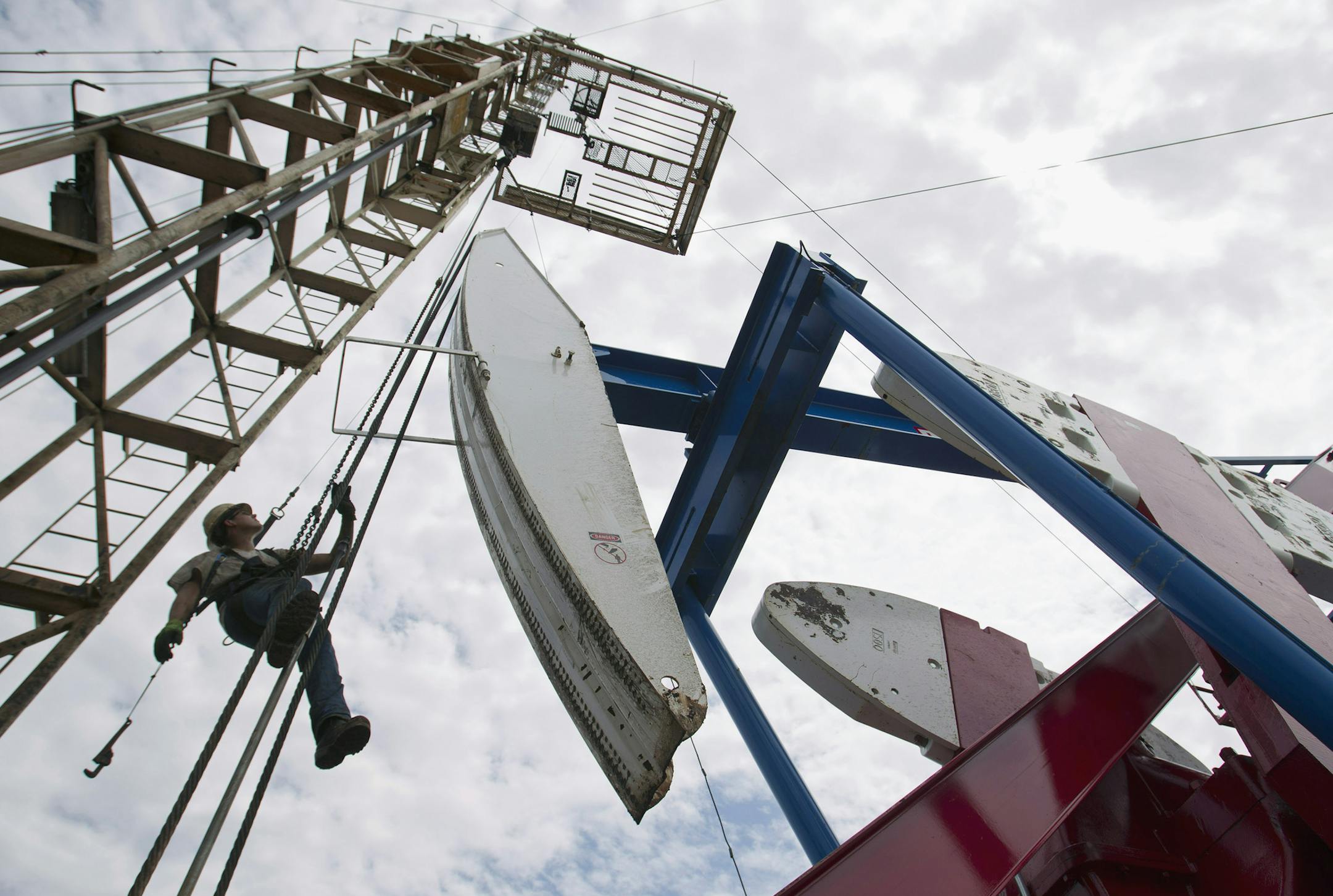 FILE - In this July 26, 2011, file photo, a worker hangs from an oil derrick outside of Williston, N.D. State data show that 1 billion barrels of oil have been produced from the rich Bakken shale formation in western North Dakota and eastern Montana. Data show that North Dakota has tallied 852 million barrels of Bakken crude, and Montana has produced about 151 million barrels. (AP Photo/Gregory Bull, File) ORG XMIT: CER603