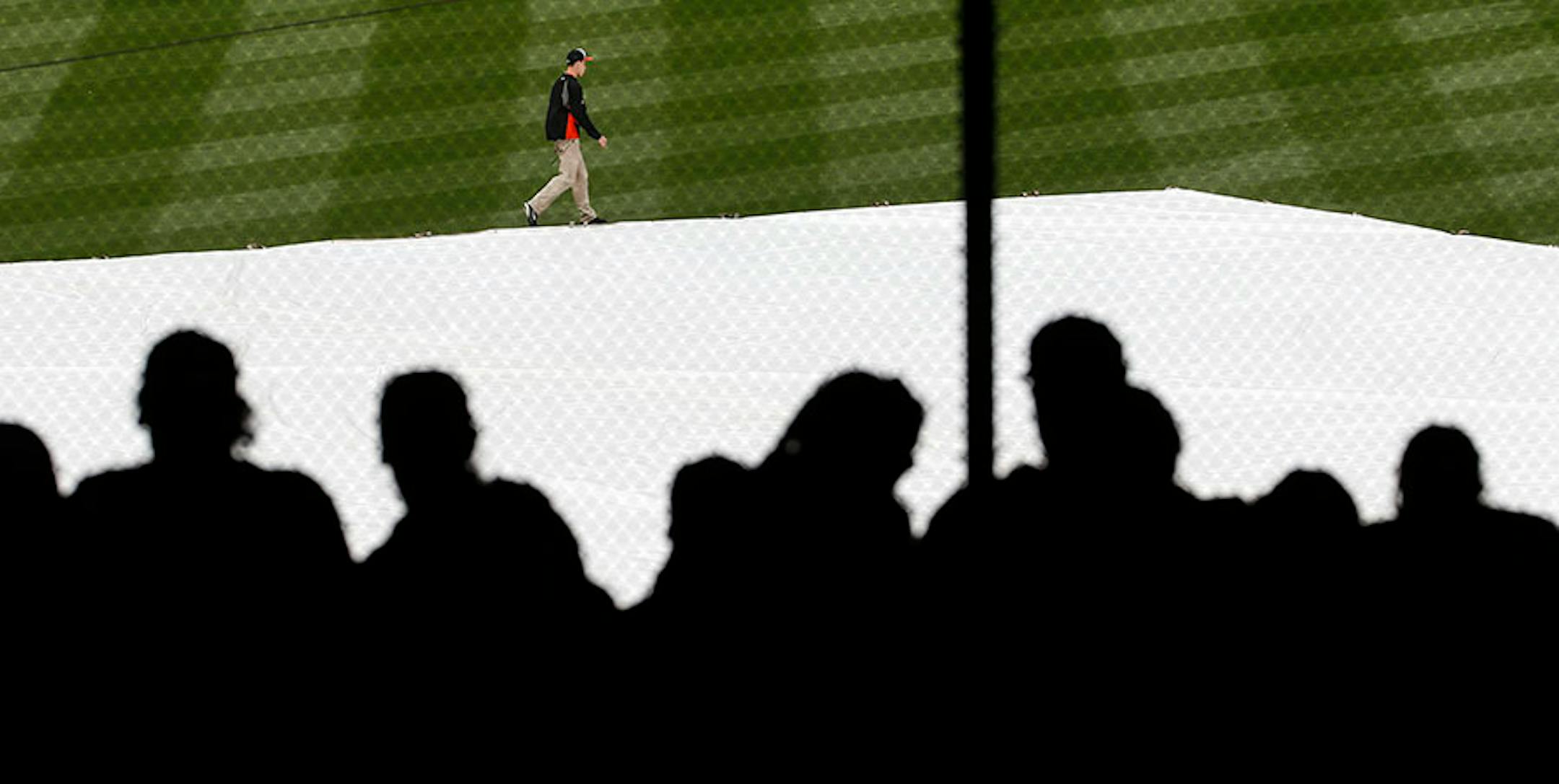 Fans sit in the stands as a groundskeeper walks past a tarp covering the infield during a rain delay before an opening day baseball game between the Baltimore Orioles and the Minnesota Twins in Baltimore, Monday, April 4, 2016. (AP Photo/Patrick Semansky)