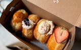 Four brioche stuffed doughnuts in a box with Thai tea, blackberry, rose lychee and strawberry black sesame flavors.