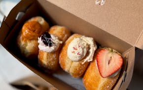 Four brioche stuffed doughnuts in a box with Thai tea, blackberry, rose lychee and strawberry black sesame flavors.