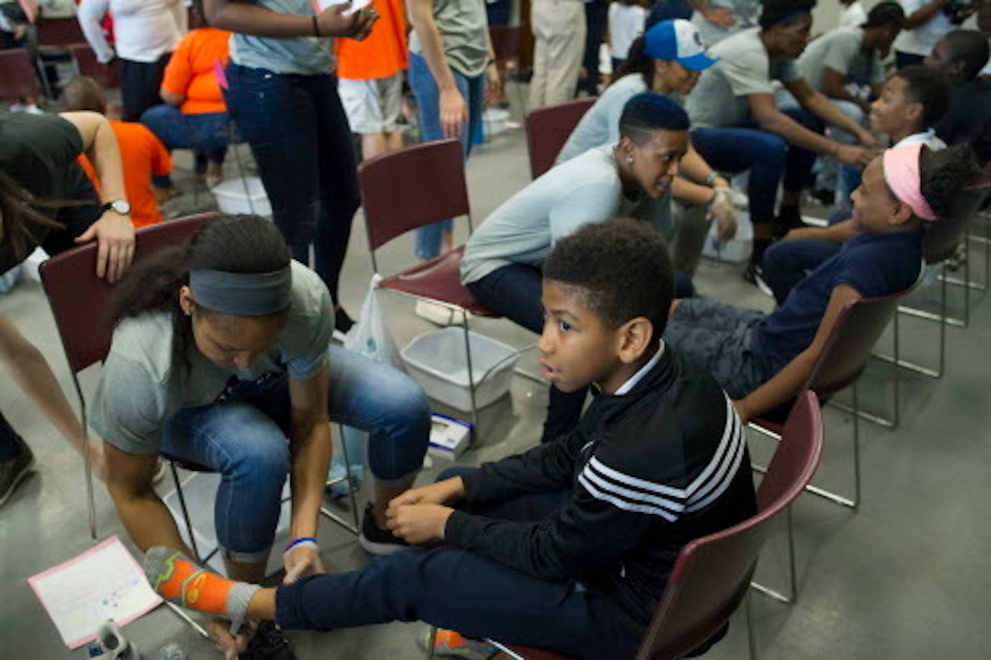 WNBA Champion Minnesota Lynx Forward Maya Moore removes a student's socks before washing his feet at Payne Elementary School in Washington, Wednesday, June 6, 2018. Payne Elementary has the highest homeless student population in the district. (AP Photo/Cliff Owen)