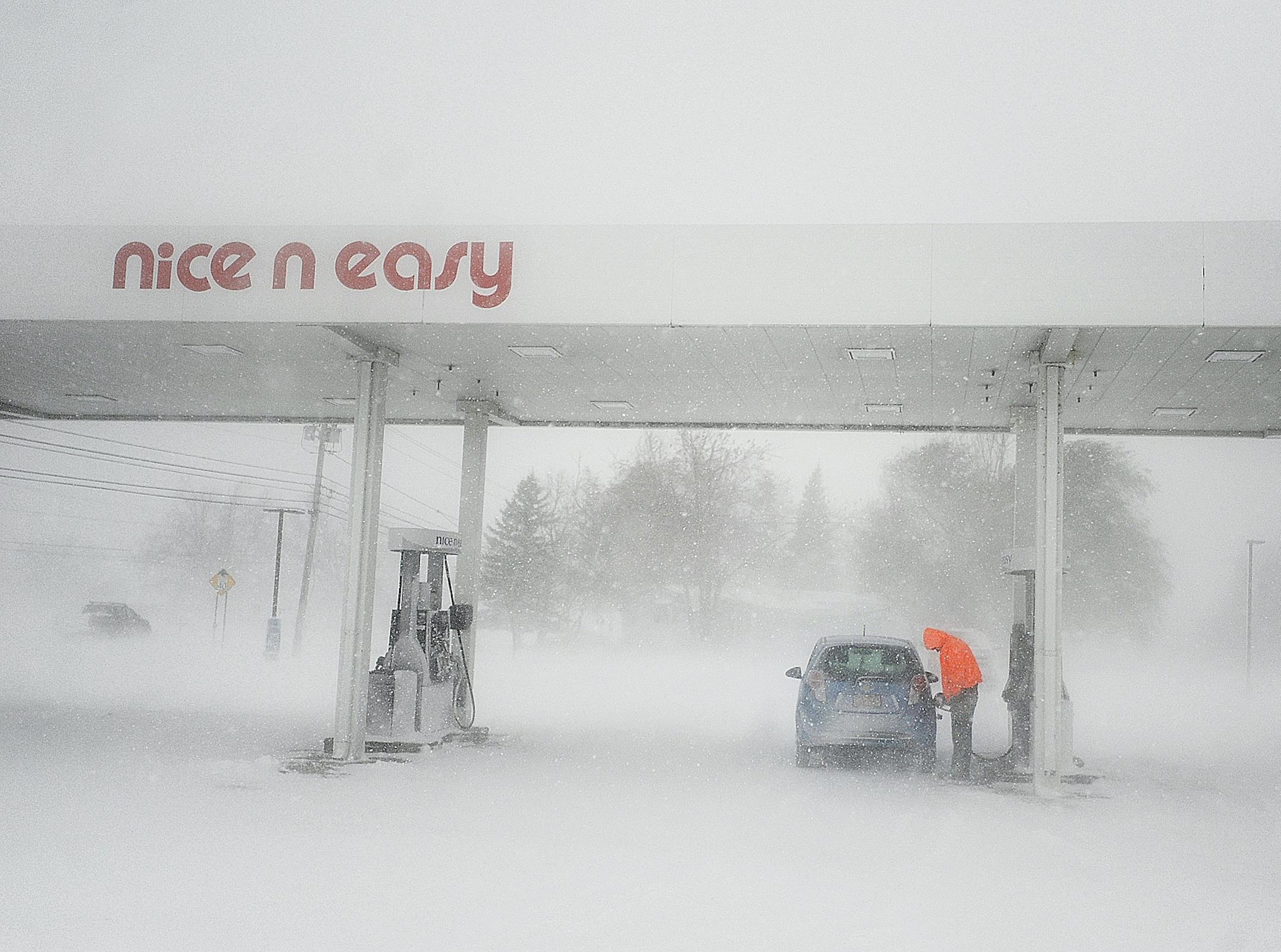In a Tuesday, Nov. 18, 2014 photo, a man puts gas in his tank as snow falls at a gas station on New York State Route 12F near Brownville, N.Y. A ferocious lake-effect storm left the Buffalo area buried under 6 feet of snow, trapping people on highways and in homes, and another storm expected to drop 2 to 3 feet more was on its way. (AP Photo/The Watertown Daily Times, Justin Sorensen) SYRACUSE OUT