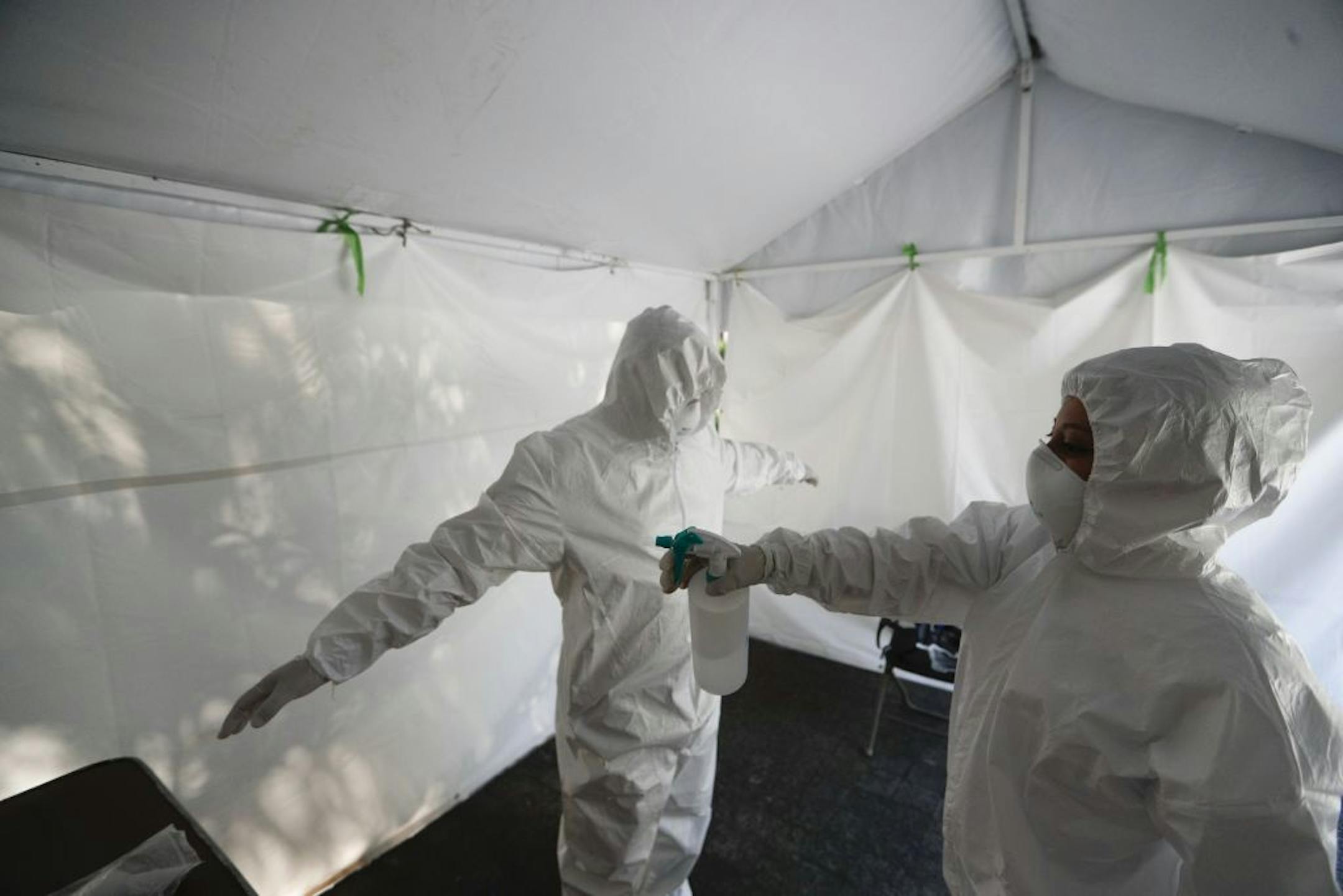 A healthcare worker disinfects a colleague at the end of a day of collecting sample to test for the new coronavirus inside a mobile diagnostic tent, in the Coyoacan district of Mexico City, Friday, Nov. 13, 2020. Mexico City announced Friday it will order bars closed for two weeks after the number of people hospitalized for COVID-19 rose to levels not seen since August.