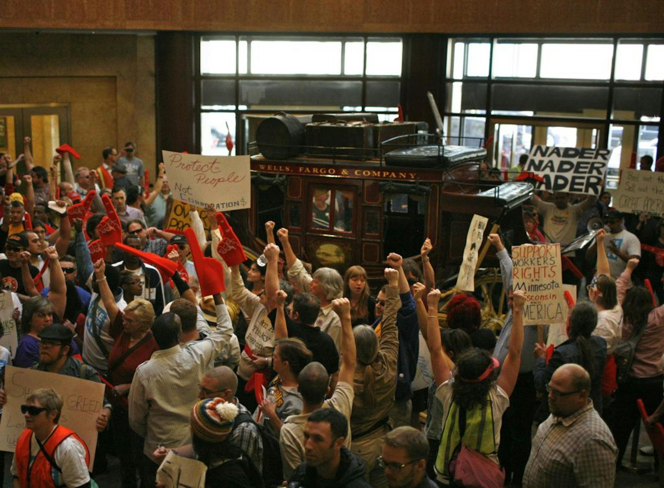 Folks from the OccupyMN gathering in addition to about two busloads of folks including union members, retirees, students, the unemployed, the employed and others marched to Wells Fargo Bank at Marquette and 6th St. over the lunch hour Tuesday. They briefly occupied the lobby, surrounding the stagecoach, chanting and raising their arms and fists in the air. They then exited the building and returned to HCGC Plasza by a different route, led the whole way by Minneapolis police controlling intersect