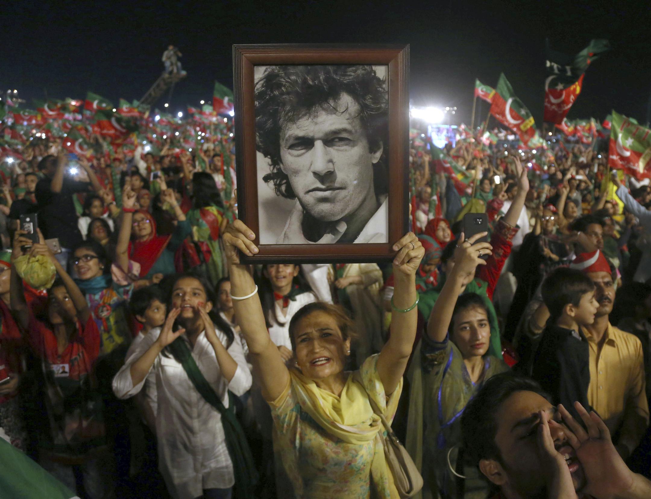 FILE - In this July 22, 2018, file photo, a woman supporter of Tehreek-e-Insaf party raises a picture of her party's leader Imran Khan during an election campaign rally in Karachi, Pakistan. Former cricket star Khan may be on the verge of victory in Pakistanís parliamentary elections. Over the years, he has parlayed his celebrity into a political career, picking up the support of the military and a conservative, religious base despite the gossip that swirls around him. (AP Photo/Shakil Adil