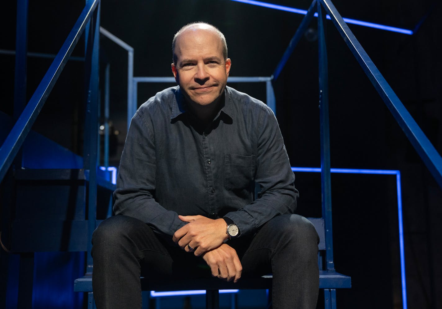 Portrait of Peter Rothstein sitting on scaffolding in darkened theater.