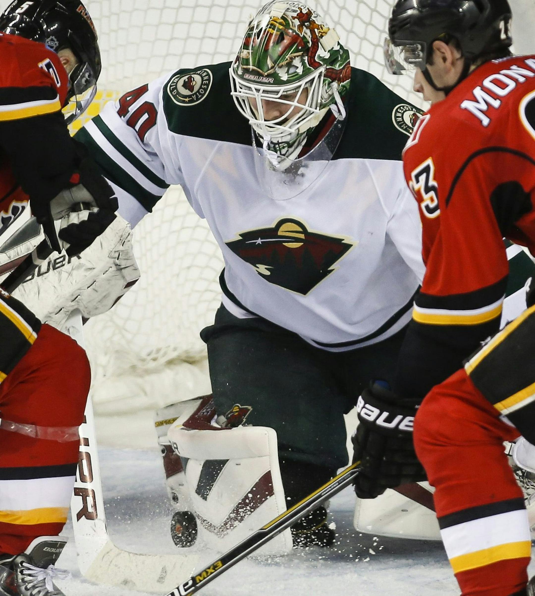 Minnesota Wild goalie Devan Dubnyk, center, pounces on the puck as Calgary Flames Mark Giordano, left, and Sean Monahan try to score during the second period of an NHL hockey game, Wednesday, Feb. 18, 2015 in Calgary, Alberta. (AP Photo/Canadian Press, Jeff McIntosh)