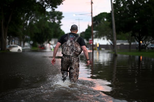 Logan Hortop of Faribault wades through knee-deep water on his way back to his truck after helping some friends deal with flooding Monday in Watervill