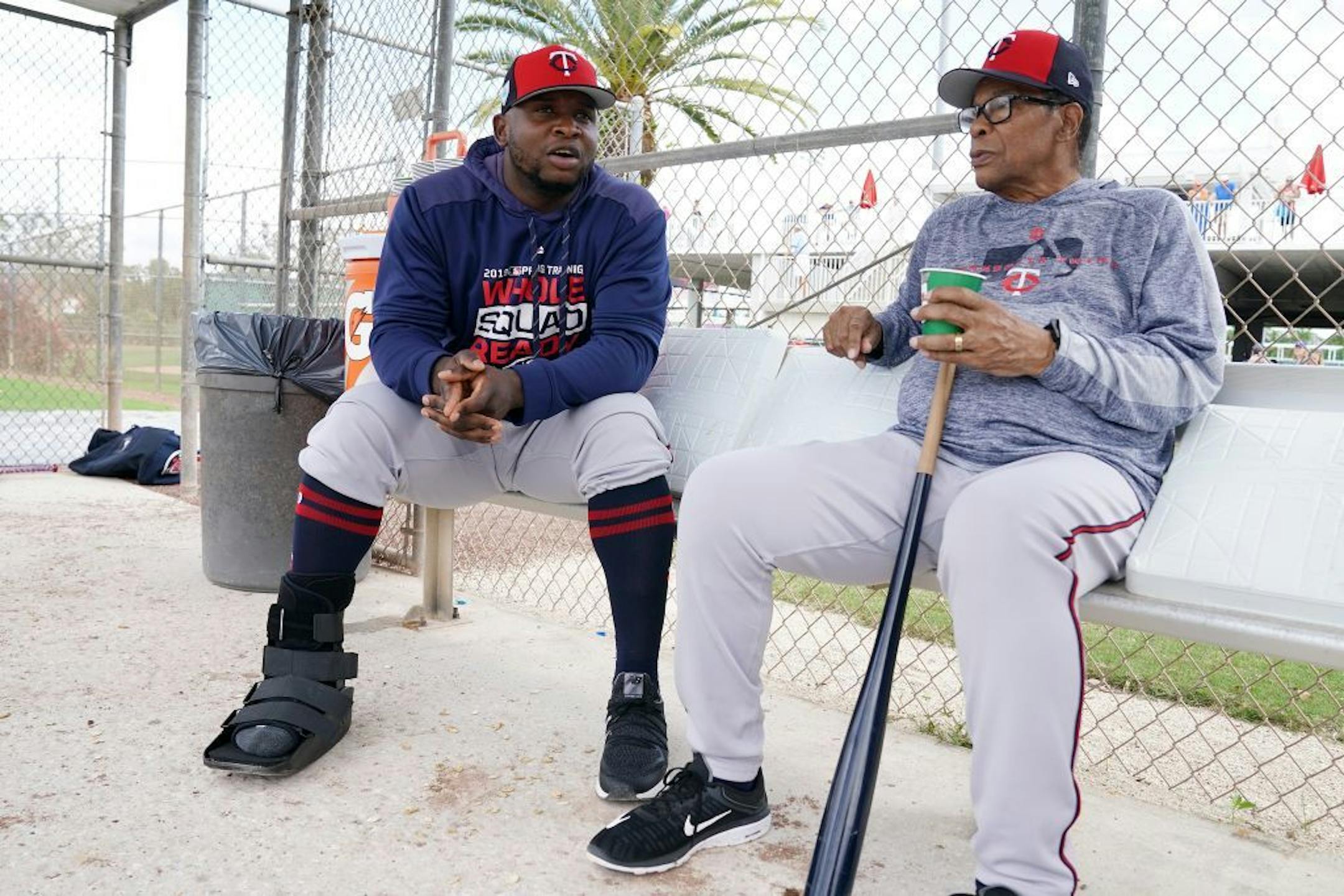 Minnesota Twins third baseman Miguel Sano (22) talked with Twins hall of famer Rod Carew (29) in the dugout at the practice field as he sat out another day of workouts wearing a boot on his right foot Wednesday.