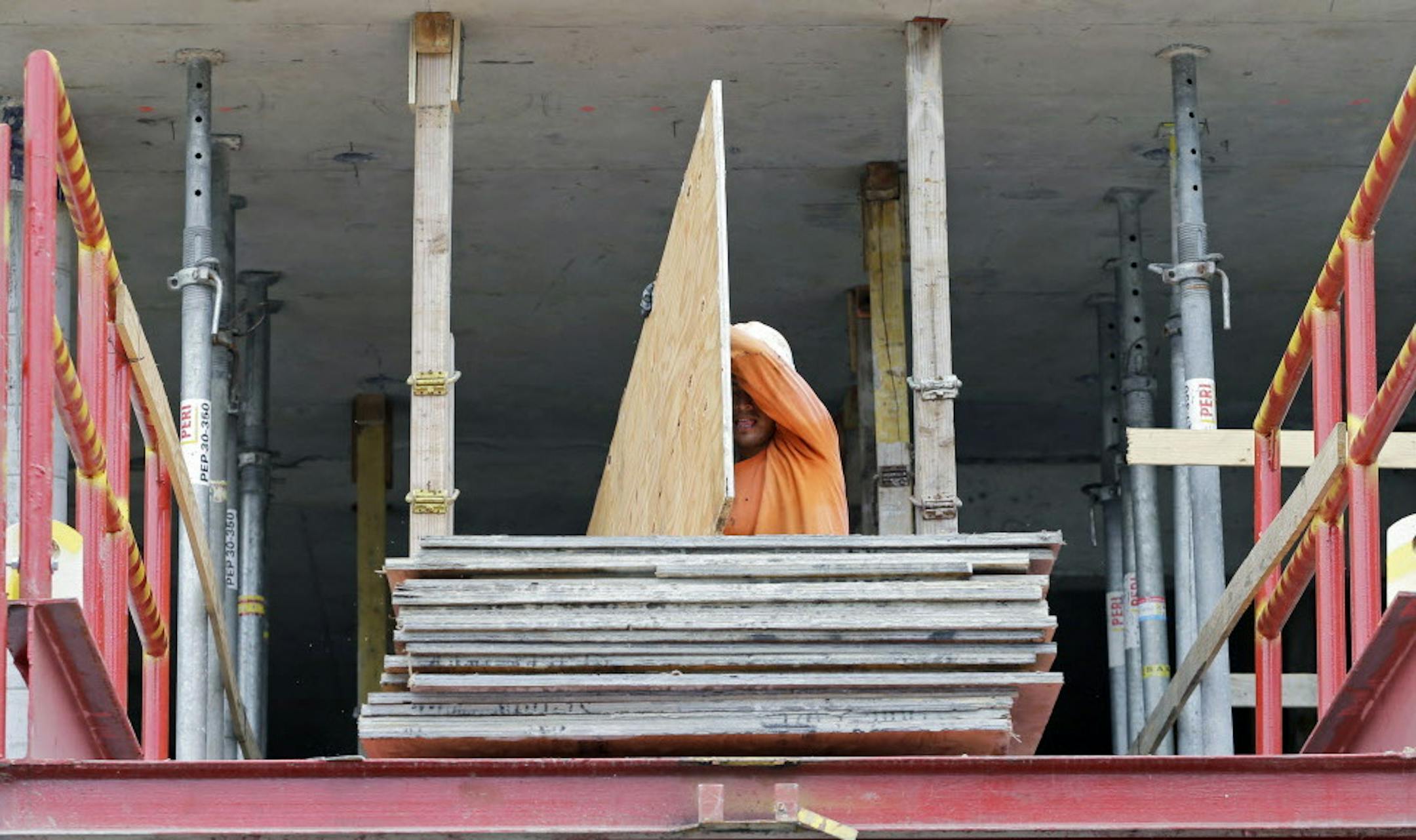 In this photo taken July 22, 2014, a construction worker carries a sheet of plywood at the site of a 36-floor high rise condominium in Miami. The National Association of Home Builders reports on sentiment among U.S. builders on Monday, Aug. 18, 2014. (AP Photo/Alan Diaz)