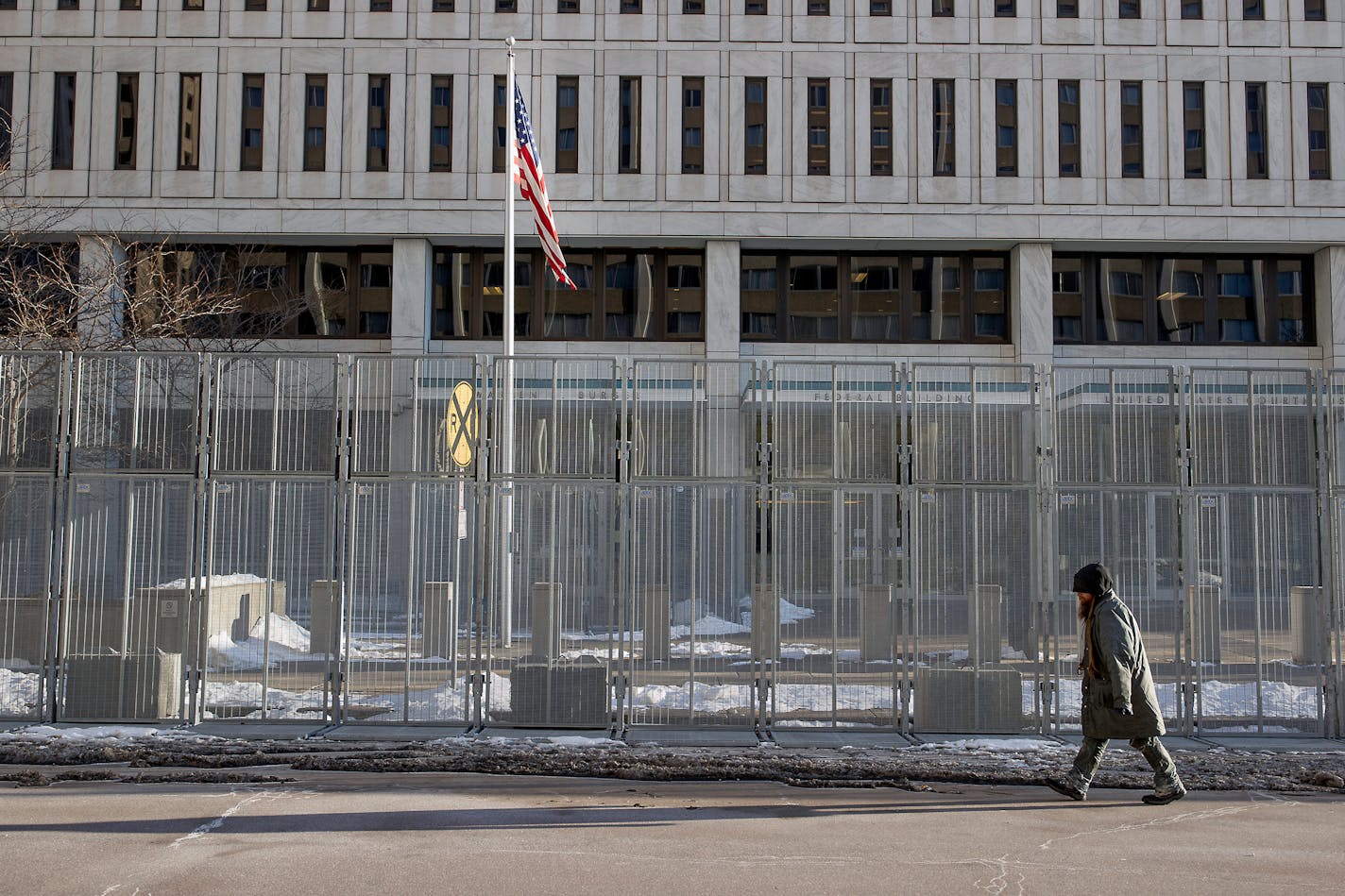 A pedestrian makes his way in front of a gated Warren E. Burger Federal Building as jury selection begins in St. Paul, Minn., Thursday, Jan. 20, 2021. Jury selection began Thursday in the federal trial of three Minneapolis police officers charged in George Floyd's killing, with the judge stressing repeatedly that fellow Officer Derek Chauvin's conviction on state murder charges and guilty plea to a federal civil rights violation should not influence the proceedings. (Elizabeth Flores/Star Tribune via AP)