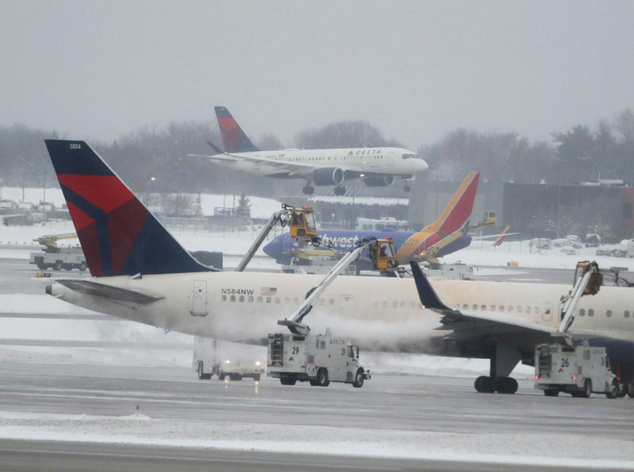 A Delta flight approaches Minneapolis-St. Paul International Airport as another is de-iced, ahead of more snow and sleet Saturday.