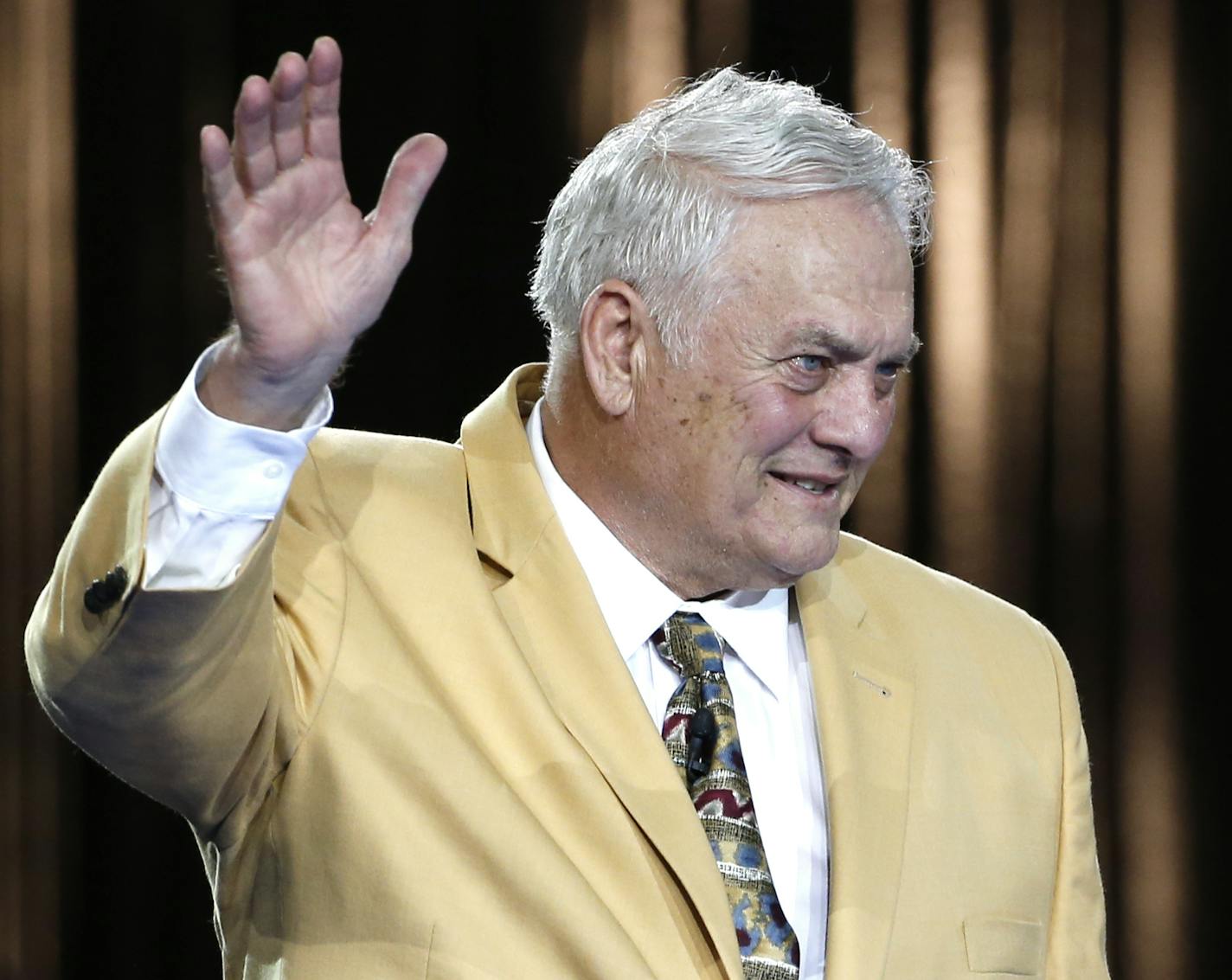 Pro Football Hall of Fame inductee Mick Tingelhoff waves after slipping on his gold jacket during the Gold Jacket Ceremony in Canton, Ohio, Thursday, Aug. 6, 2015. (AP Photo/Gene J. Puskar)