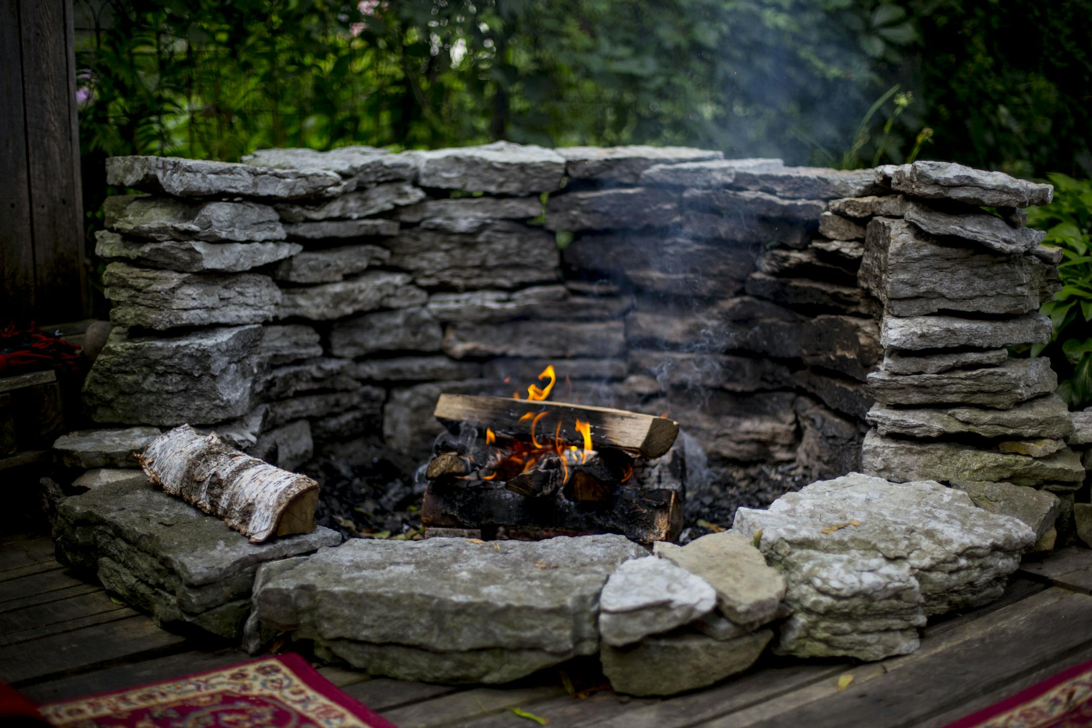 A stone firepit with wooden seating areas around it sits beside the pond.