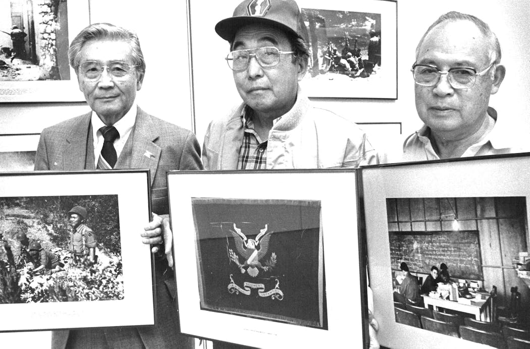 In this 1984 photo, Tosh Abe, left, with a photo showing battle conditions in Burma where he served; Nob Kimura with a photo of the design of flag for the 442nd Regimental Combat Team; and Frank Yanari with a classroom scene from Camp Savage.