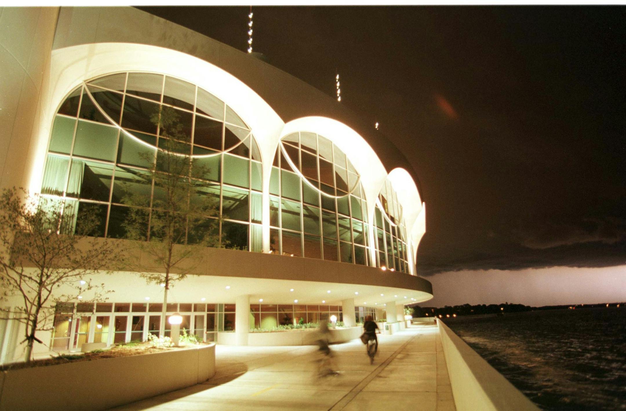 -- Lightening from an approaching storm lights the horizon as bicyclists ride along the lakeside walkway and bike path next to Monona Terrace.