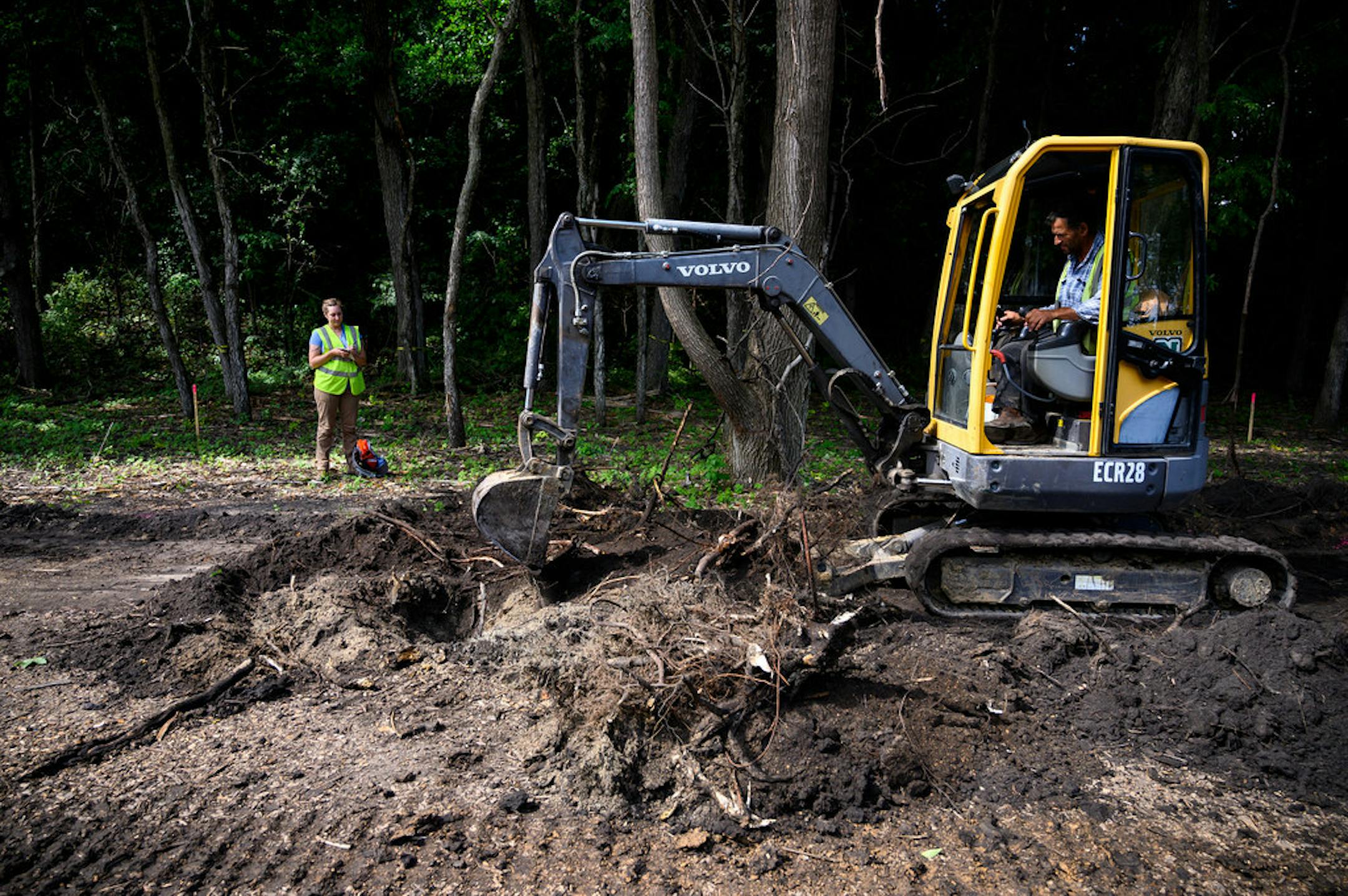 Archaeologist Kelly Wolf, left, with Blondo Consulting, took photos and notes as contractors used heavy machinery to dig up a trail on Coney Island of the West.