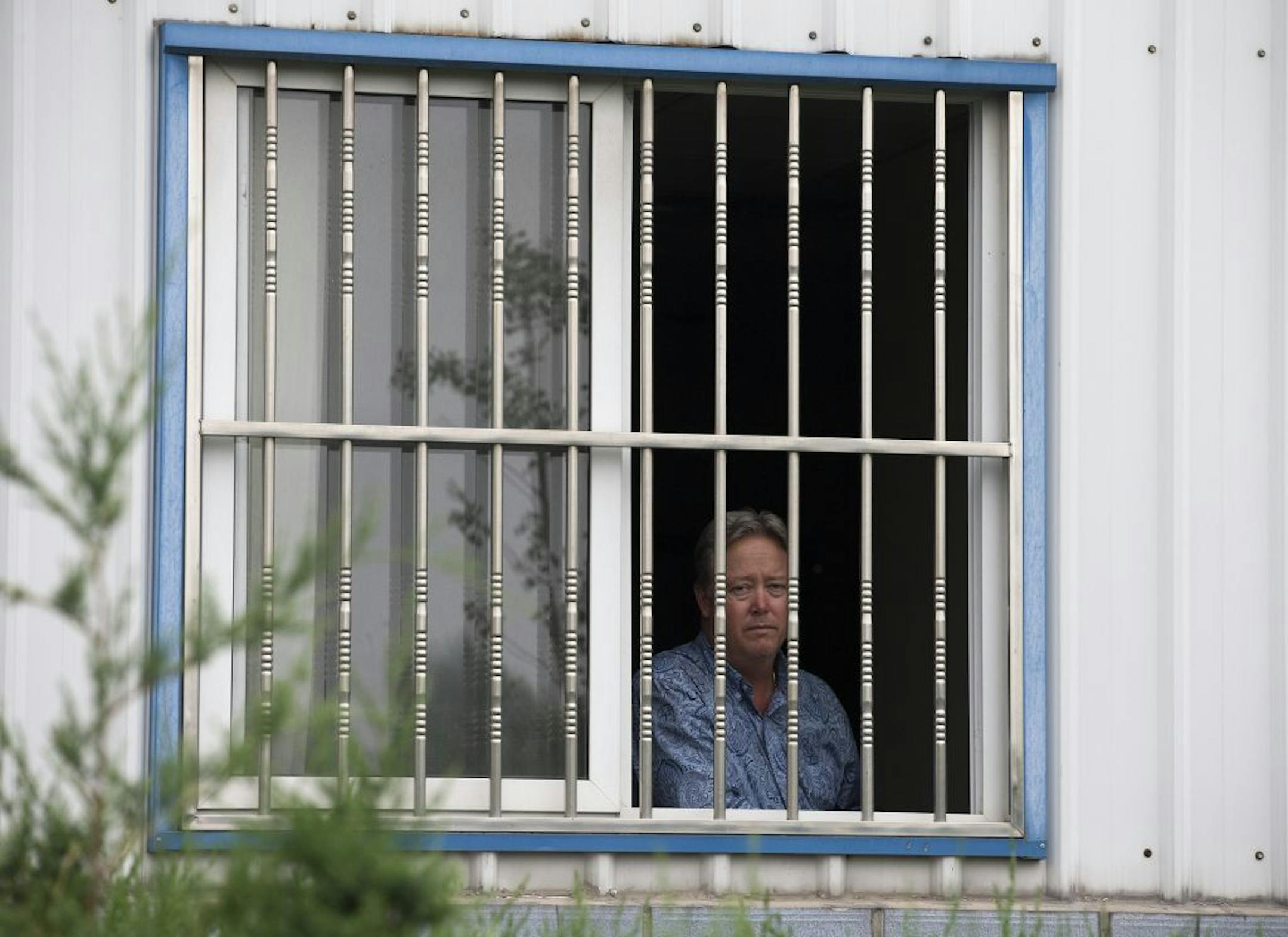 American Chip Starnes, co-owner of Specialty Medical Supplies, looks out from a window after he was held hostage by workers inside his plant at the Jinyurui Science and Technology Park on the outskirts of Beijing, China Monday, June 24, 2013.