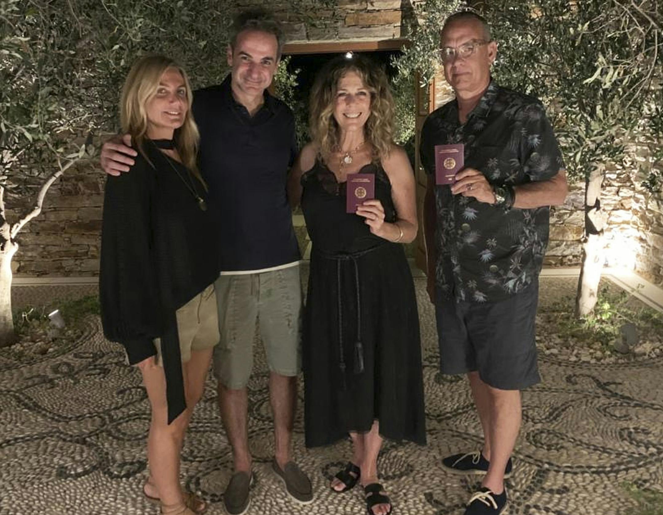 In this photo provided by Greek Prime Minister's Office, Greek Prime Minister Kyriakos Mitstotakis, second left, his wife Mareva Grabowski-Mitsotaki, left, pose next to U.S. actor Tom Hanks , right, and his wife Rita Wilson holding up their new Greek passports, in the island of Antiparos, Greece on Saturday, July 25, 2020. Greece offered citizenship Hanks, Wilson, and their two children, in recognition of the family's help in assisting victims of a deadly wildfire near Athens in 2018. (Greek Pri