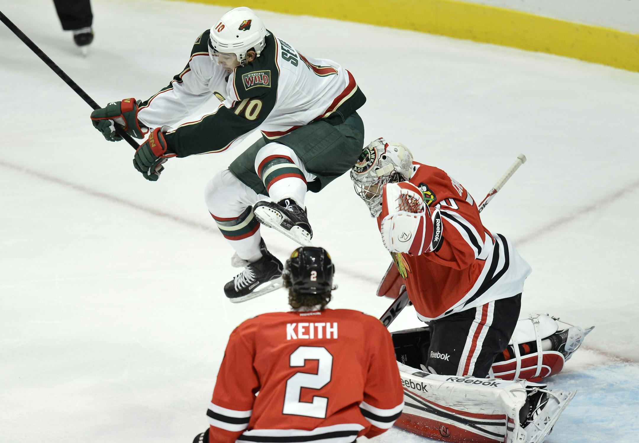 Minnesota Wild right wing Devin Setoguchi , left, leaps into the air to avoid a shot on Chicago Blackhawks goalie Corey Crawford, right, during the first period of an NHL hockey game, Tuesday, March 5, 2013 in Chicago. The Blackhawks won 5-3. (AP Photo/Brian Kersey)