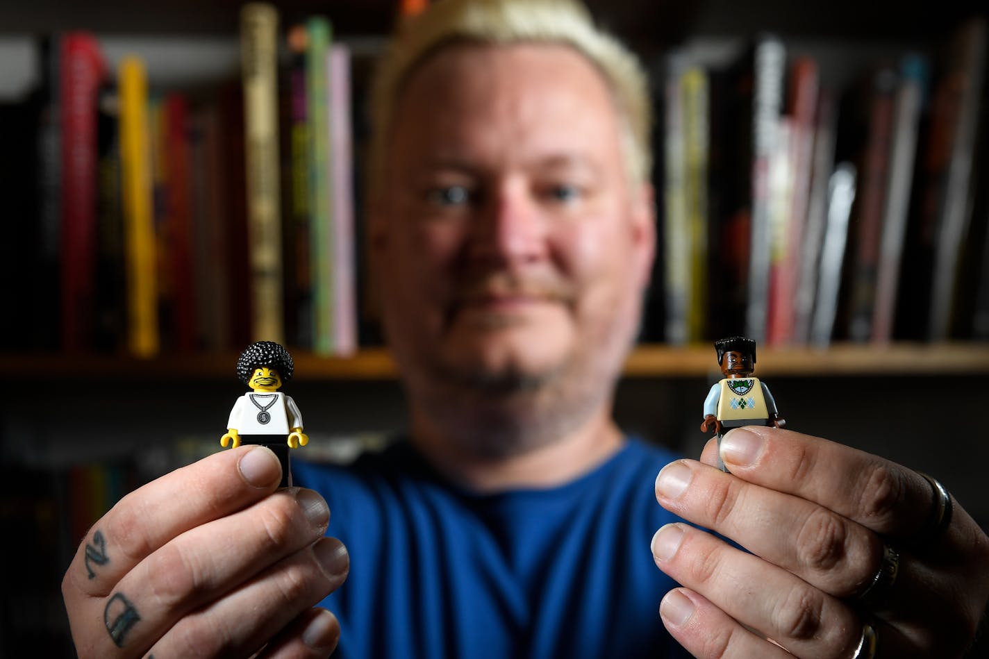 Ray Cook holds two Lego figurines, which he says "show the complex representations of blackness in Lego." The Lego on the left shows a "black skin tone in a world where they're [skin tones] all the same."