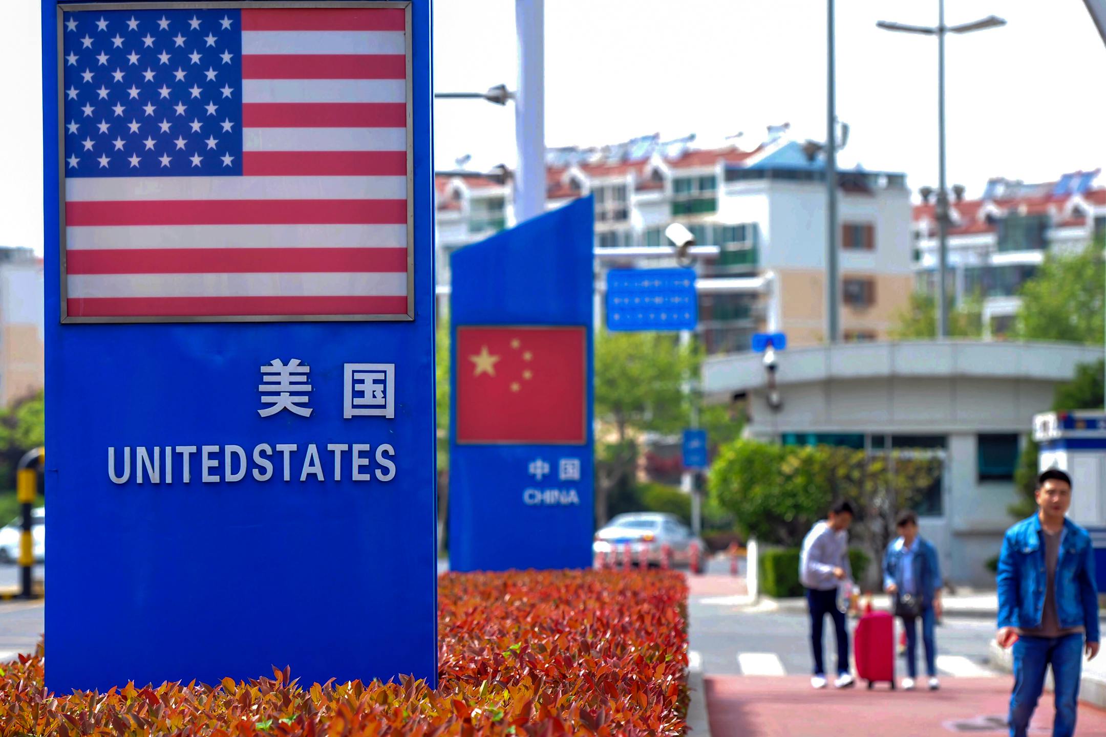 In this May 8, 2019, photo, people walk by a display boards featuring the U.S. and Chinese flags in a special trade zone in Qingdao in eastern China's Shandong province. A government spokesman says Chinese companies have expressed willingness to import U.S. farm goods as envoys prepare to meet next week for talks aimed at ending a tariff war. (Chinatopix via AP)