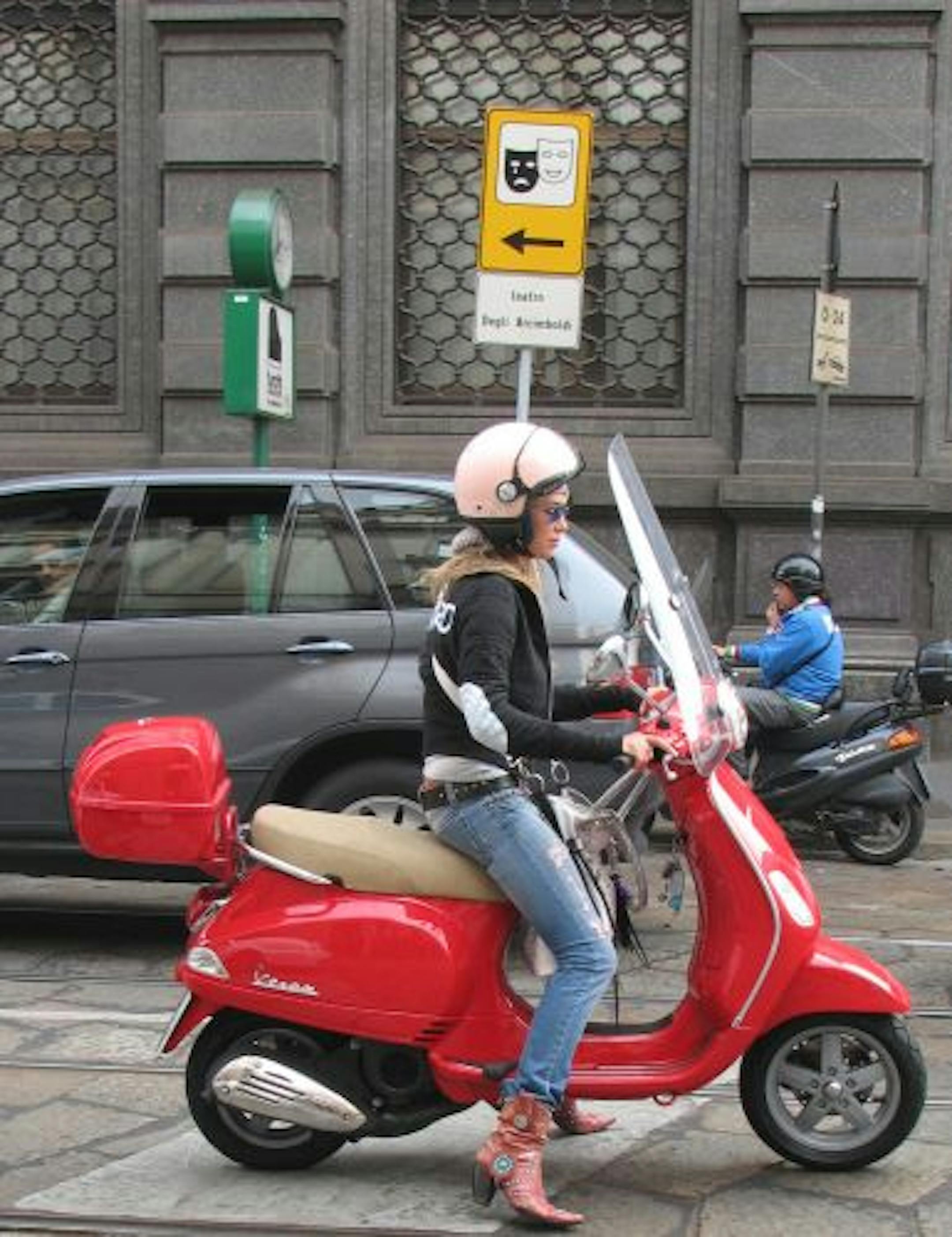 Scooters are a popular — and practical — transit option in the narrow streets of many Italian cities. Above, a young woman waits for the light to change in downtown Milan, near the famous Teatro alla Scala.