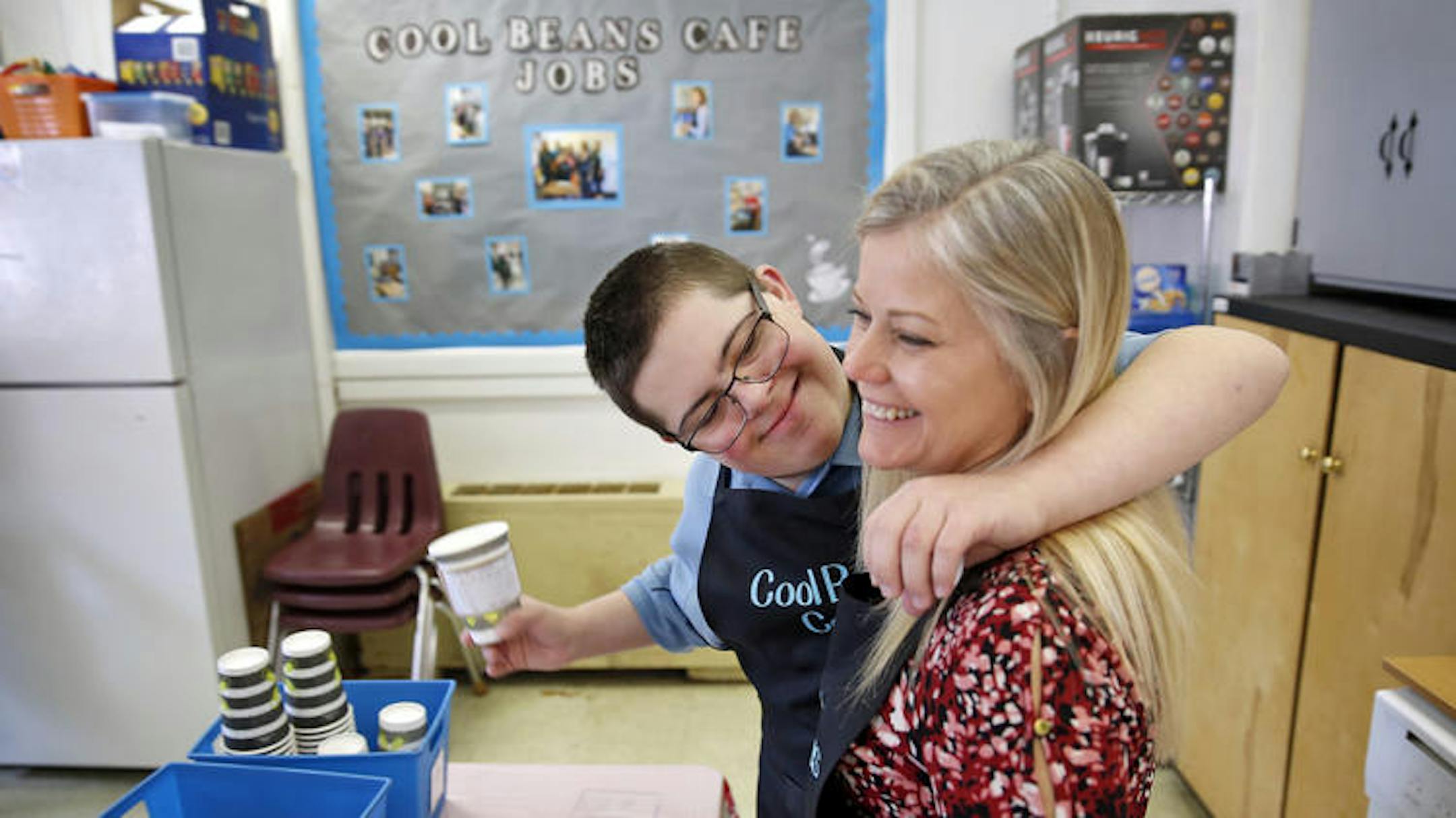 Jake Mann hugs Betsy Ferguson while working at Poquoson Middle School's Cool Beans Cafe Thursday morning March 29, 2018. Special needs students run all aspects of the coffee shop which help them get experience with job skills and social interactions outside a typical classroom environment.