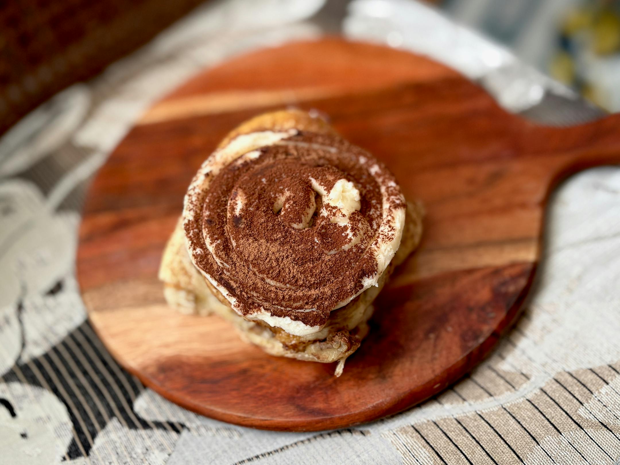 A tiramisu flavored sweet roll topped with frosting and a dusting of cocoa powder.