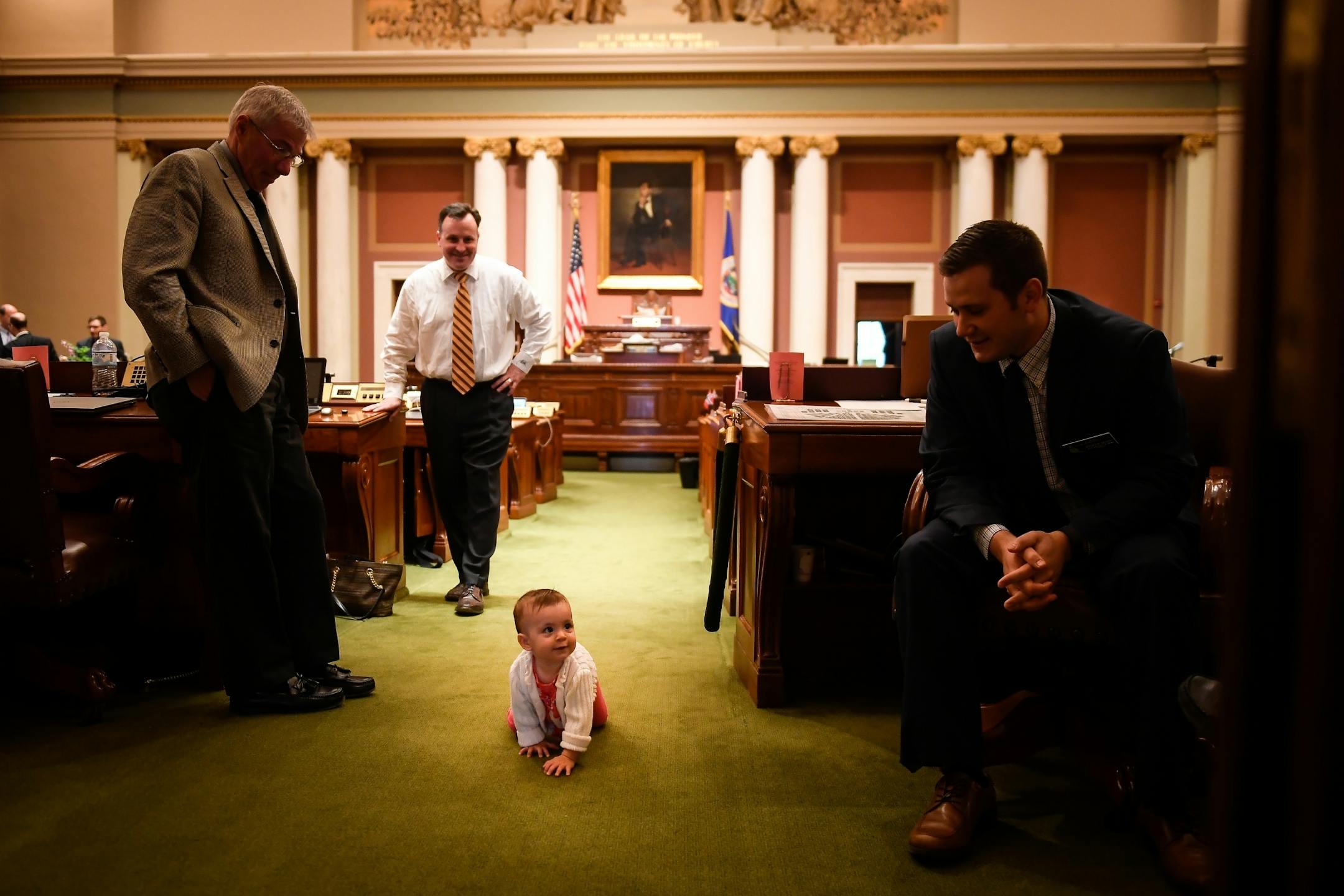 Eleanor Lesch, center, daughter of Rep. John Lesch (DFL), back center, crawled her way down the aisle of the house chamber Tuesday during a recess in the legislative special session.
