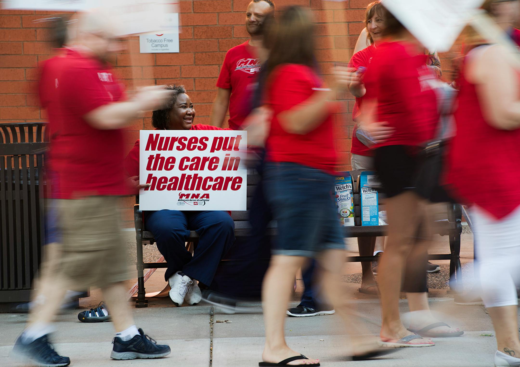 Queen Obasi holds up a sign and offers snacks to picketers as they pass by in front of United Hospital in St. Paul.