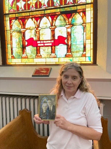 Patti-Folstad Bouley, holding a photo of her great-grandparents in frontt of a stained-glass window honoring their parents.Curt Brown