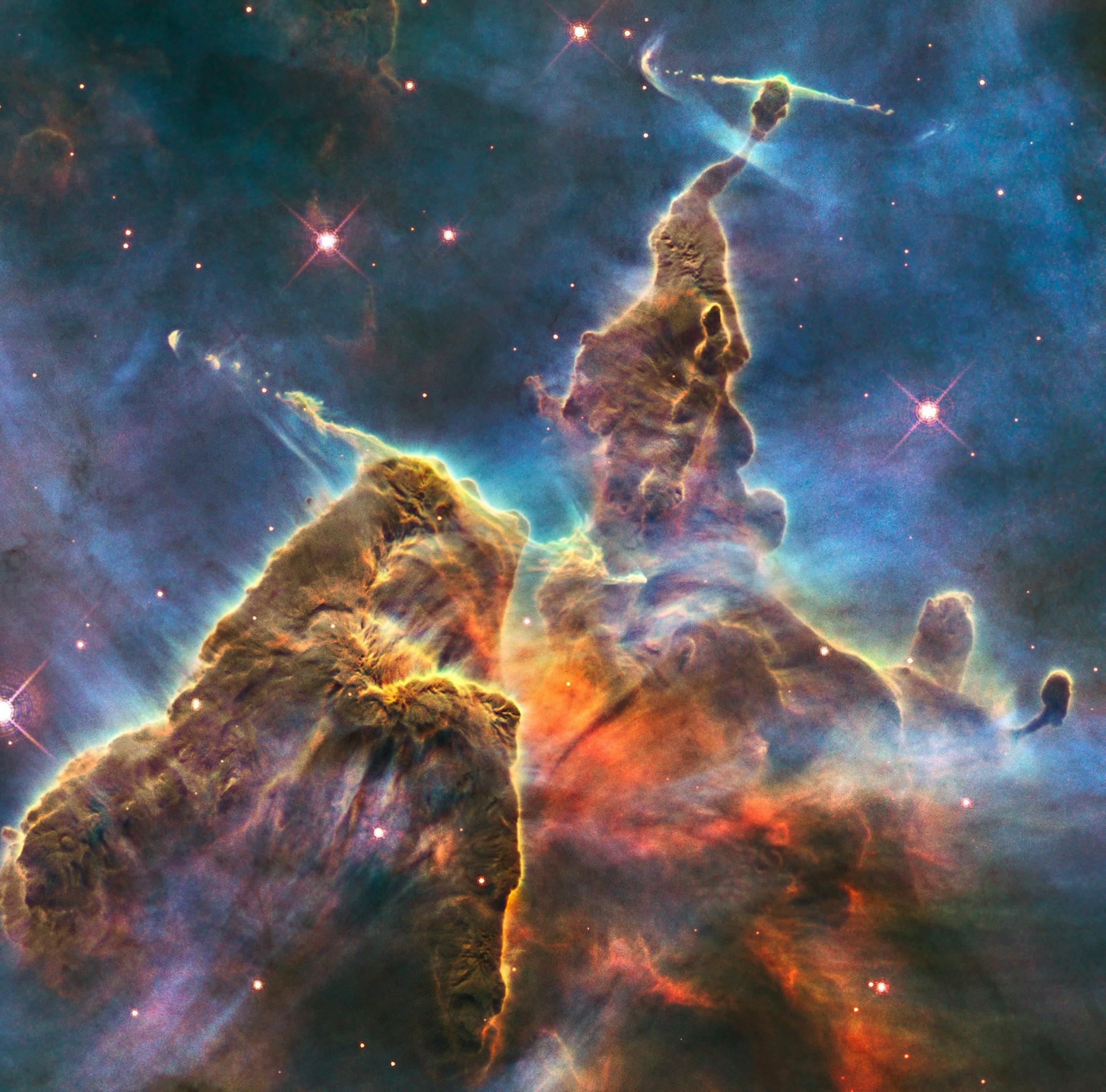 This February 2010 image made by the NASA/ESA Hubble Space Telescope shows a three-light-year-tall pillar of gas and dust in the Carina Nebula which is being eaten away by the light from nearby bright stars. Inside, infant stars fire off jets of gas that can be seen streaming from towering peaks. The stellar nursery is located 7500 light-years away in the southern constellation of Carina. The colors in this composite image correspond to the glow of oxygen (blue), hydrogen and nitrogen (green), a