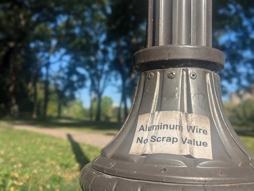 A Minneapolis light pole along West River Road with signage warning would-be copper thieves.