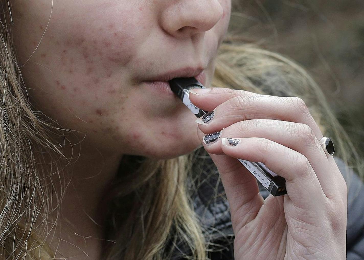 FILE - In this April 11, 2018, file photo, a high school student uses a vaping device near a school campus in Cambridge, Mass. U.S. health regulators are moving ahead with a plan to keep e-cigarettes out of the hands of teenagers by restricting sales of most flavored products in convenience stores and online.