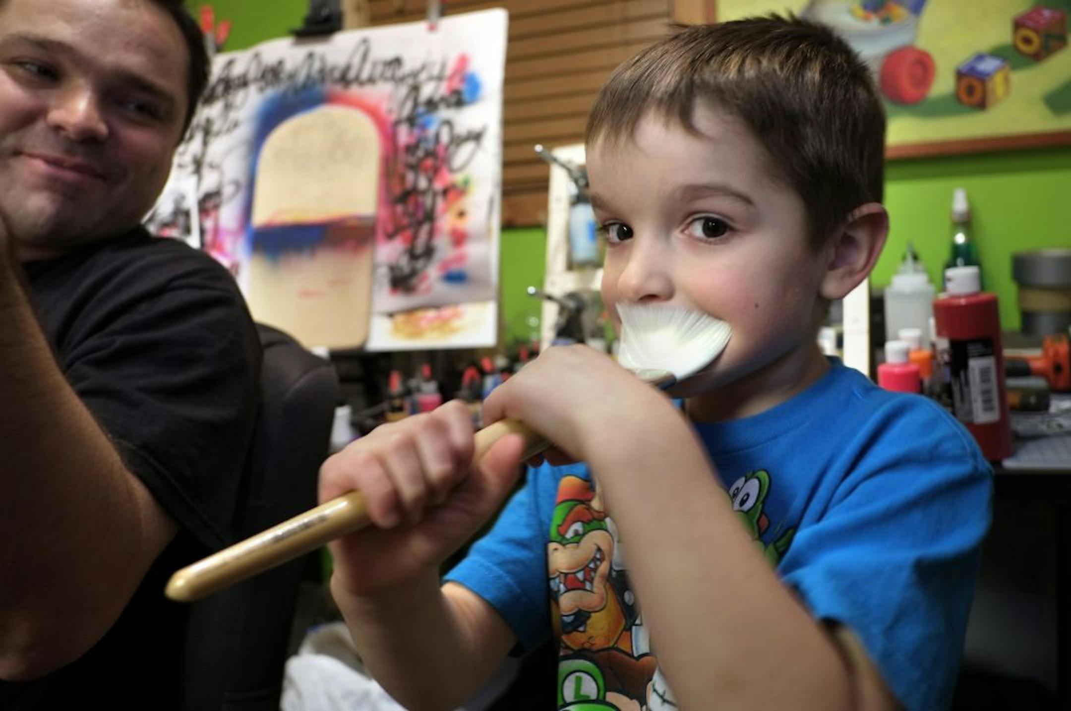 Louis Bustos spends hours with his dad, Dan, left, working on his dress designs in the family's above-the-garage art studio. The space, which had been filled with Dan's paintings and sculptures, is quickly being taken over by a storm of paper doll cutouts, pompoms and boxes of buttons and beads.