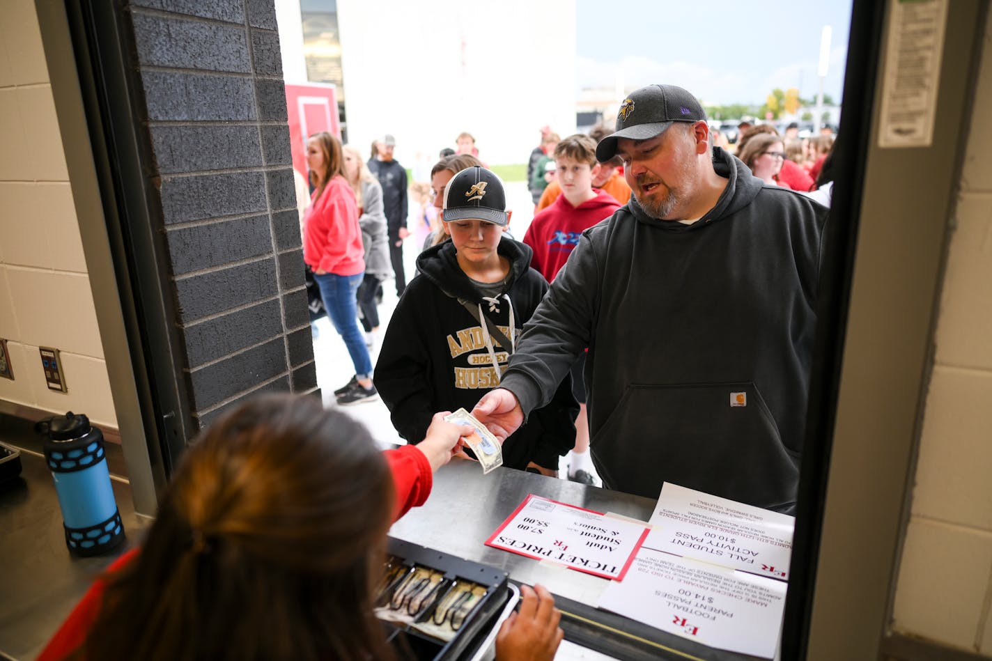 Paul Kerns, of Andover, is handed game tickets and change at the box office beside his 11-year old son, Logan, before the start of a football game between Elk River and Andover Friday, Sept. 9, 2022 at Elk River High School in Elk River, Minn. ] aaron.lavinsky@startribune.com