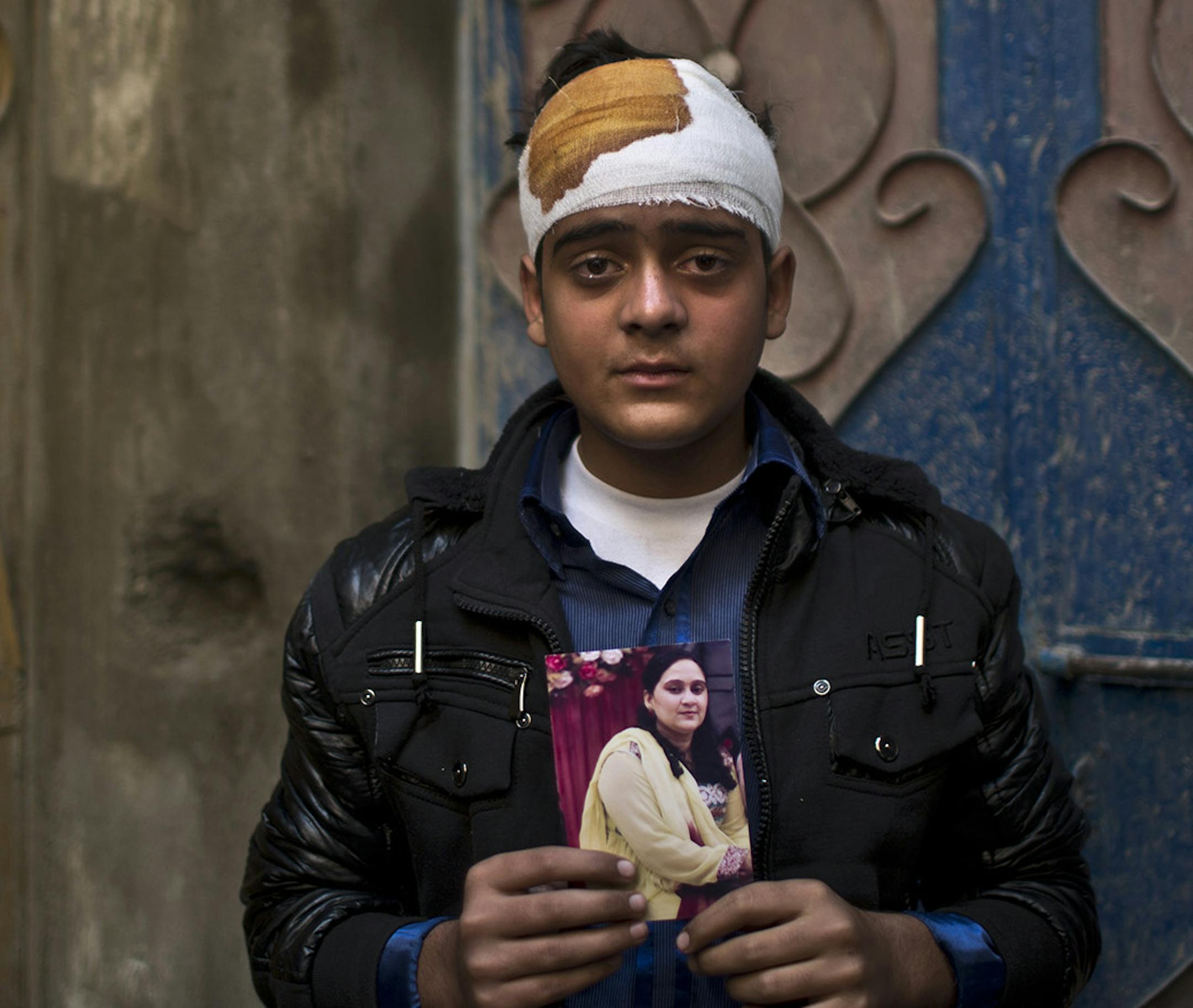 Pakistani student, Mohammad Baqair, who survived last Tuesday's Taliban attack on a military-run school and was slightly injured, poses for a picture holding a photograph of his mother a victim of the attack, who was a teacher at the school, at his home, in Peshawar, Pakistan, Thursday, Dec. 18, 2014. The Taliban massacre that killed more than 140 people, mostly children, at a military-run school in northwestern Pakistan left a scene of heart-wrenching devastation, pools of blood and young lives
